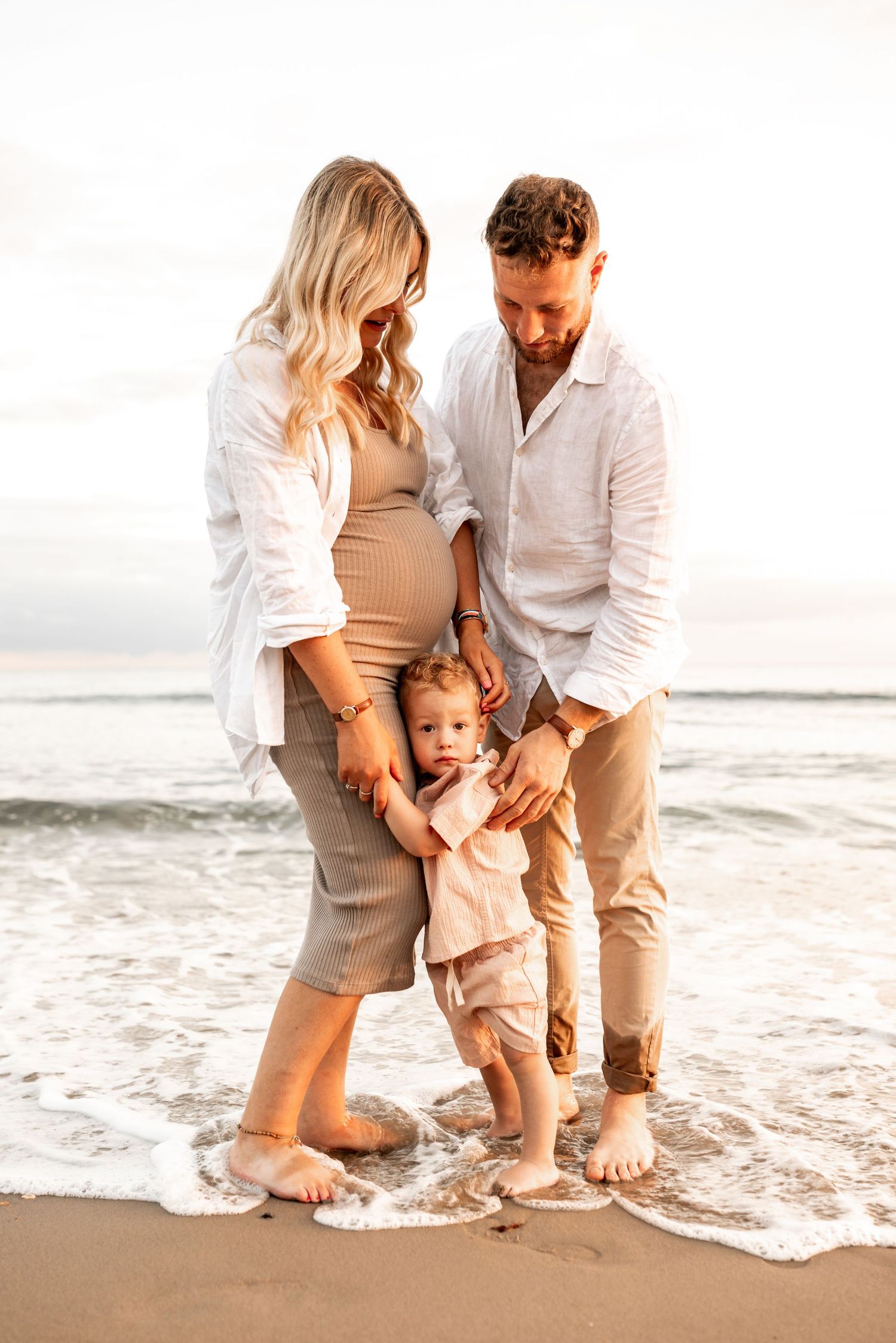 A family plays together at the beach's edge during sunset, their feet in the gentle surf.