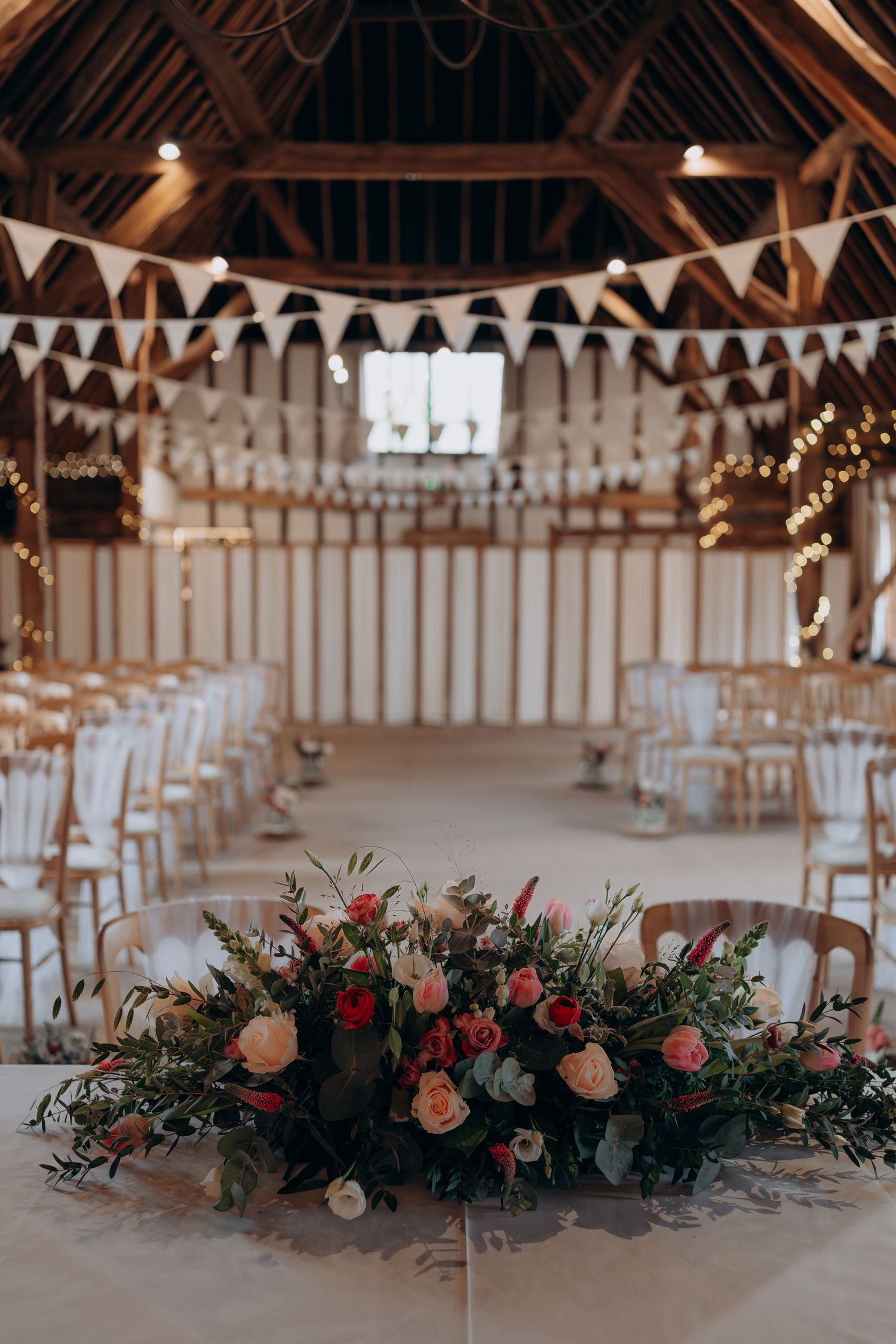 Long rustic barn venue decorated with white bunting flags and floral centerpieces for a wedding reception.