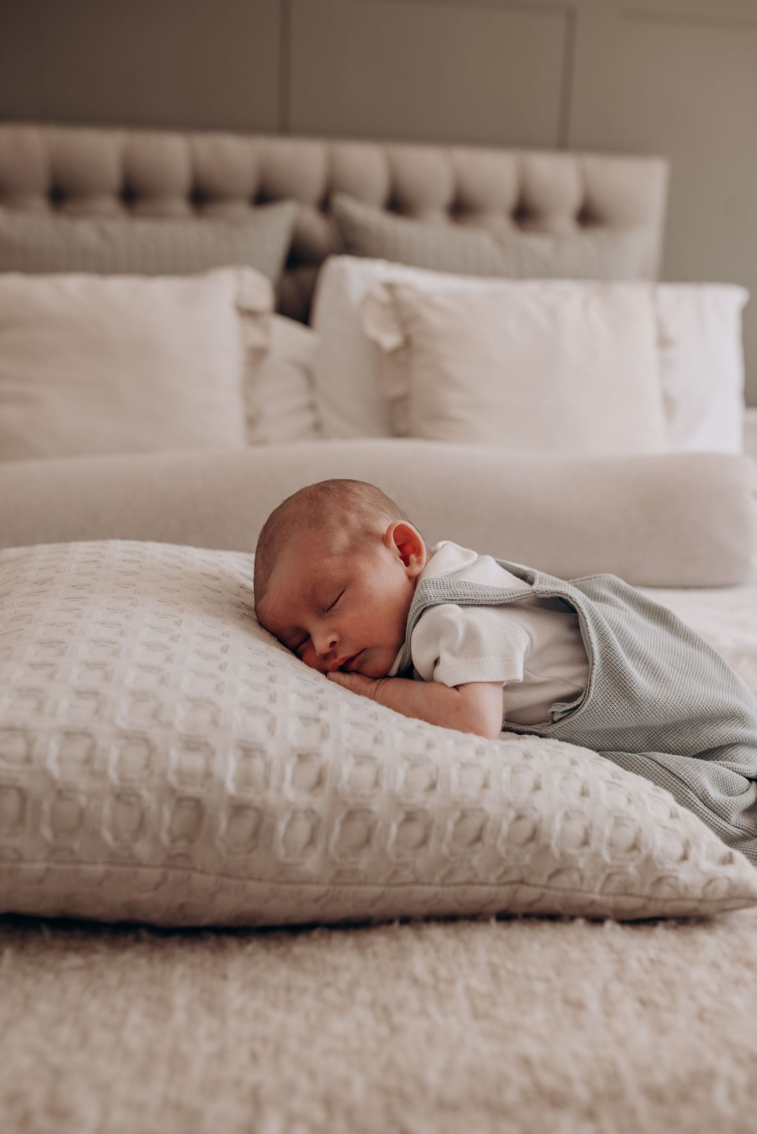 Peaceful sleeping baby in gray outfit on textured white bedding.