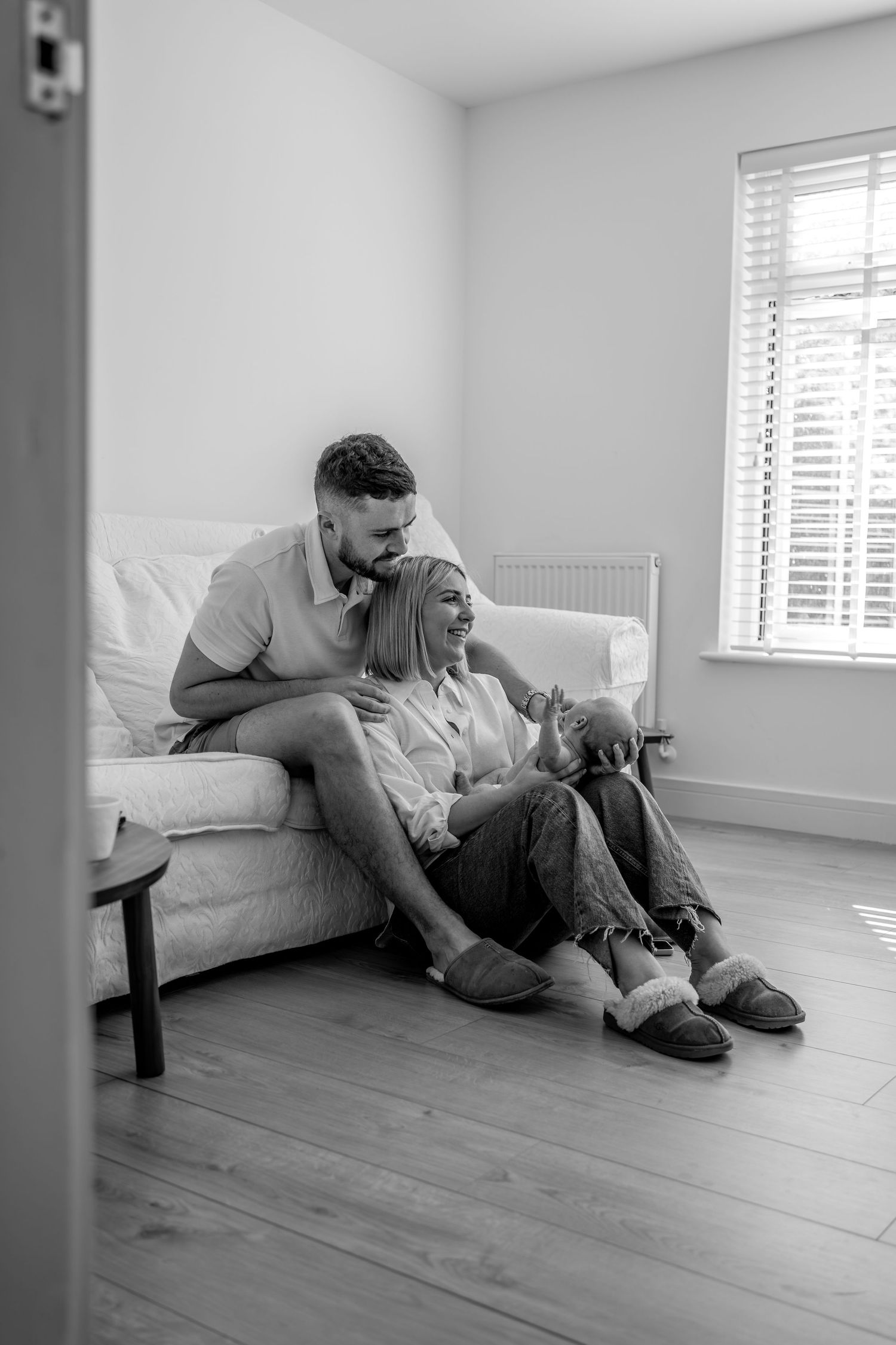 Family relaxing together on wooden floor in bright room.