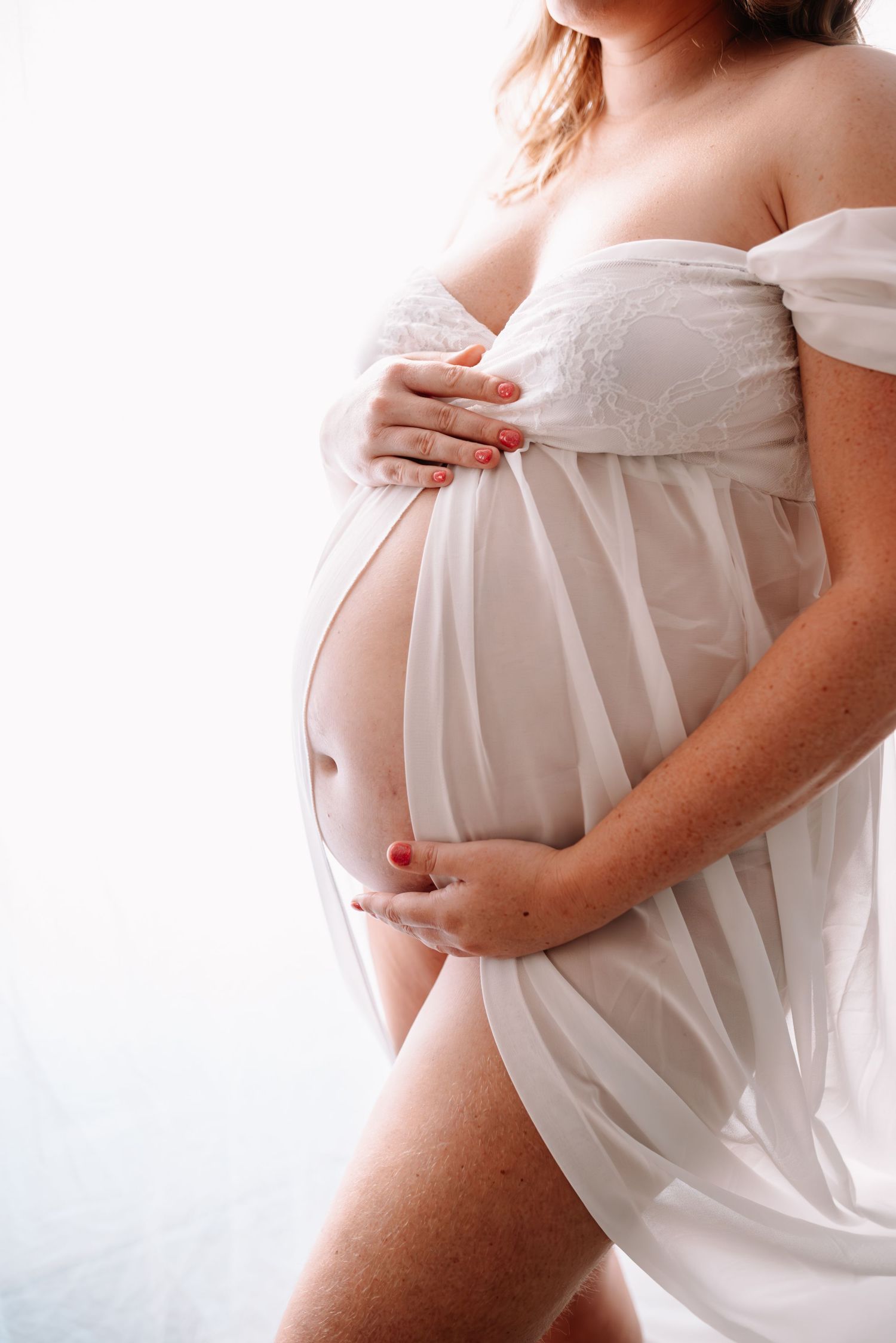 Artistic maternity photo featuring flowing white dress highlighting pregnancy silhouette.