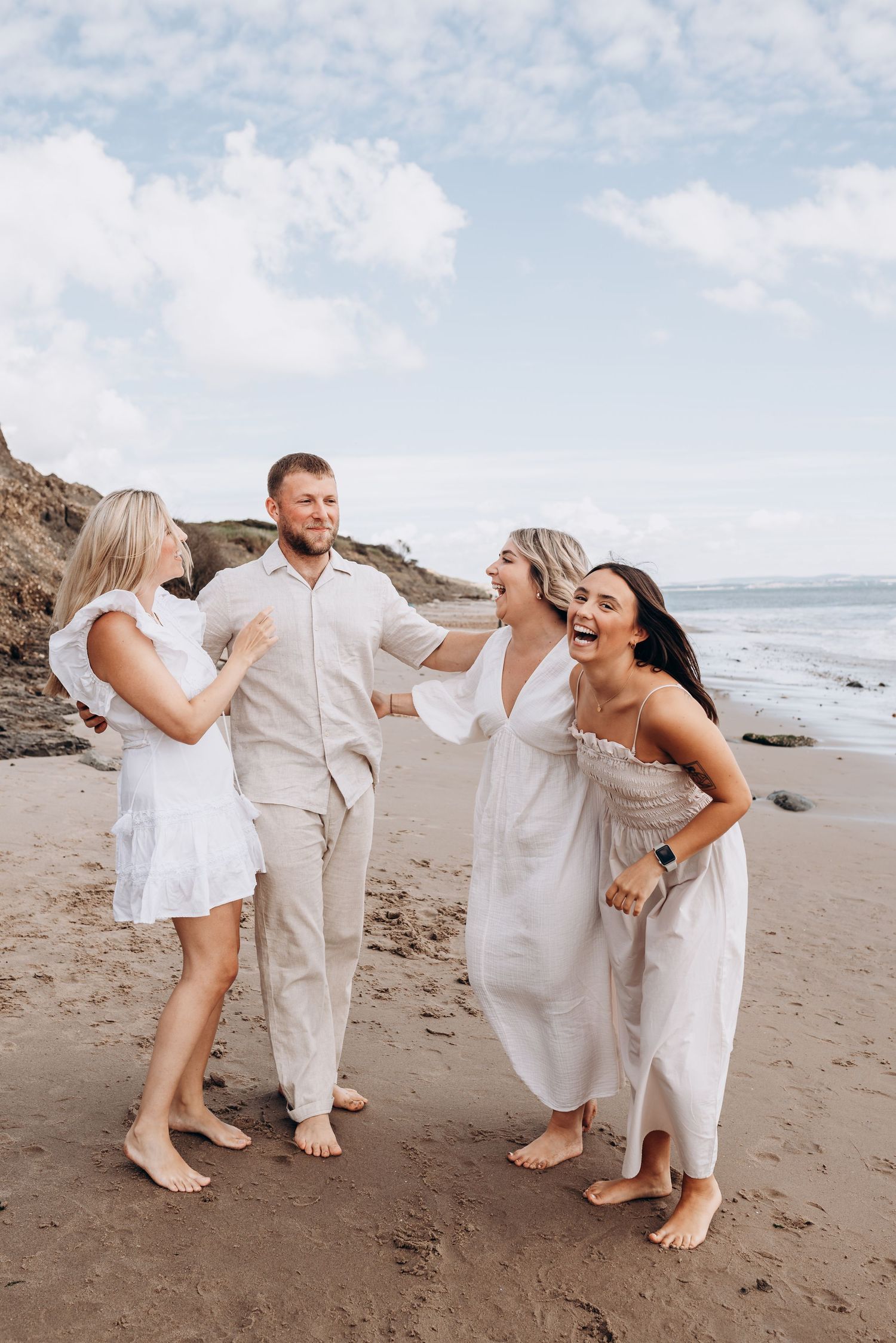 A group in white outfits laughs together on a rocky beach.