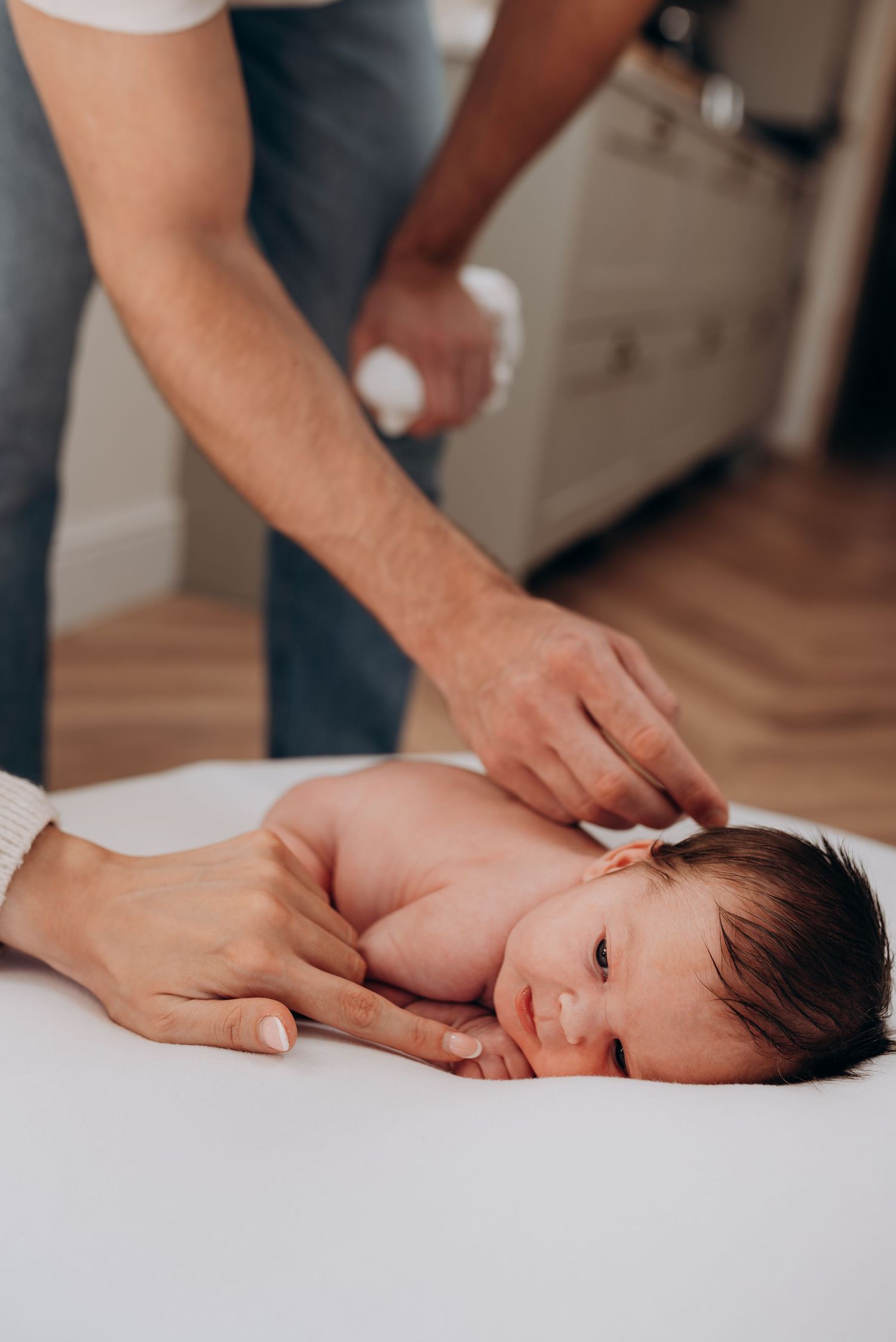 A close-up view of hands giving a gentle massage to a newborn baby lying on white bedding.