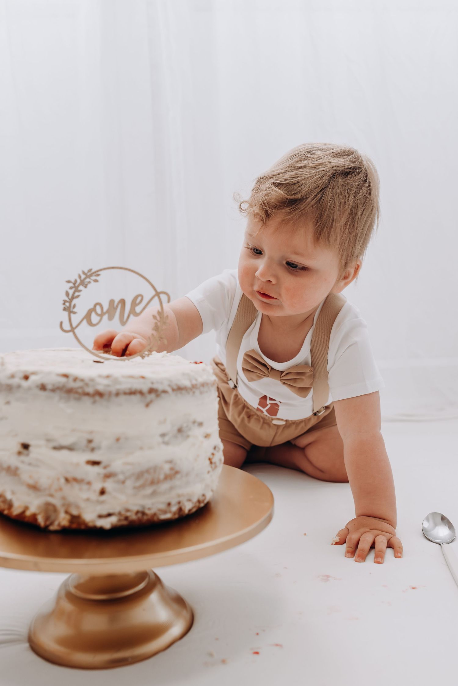 Baby exploring and tasting a white frosted cake on a gold cake stand.
