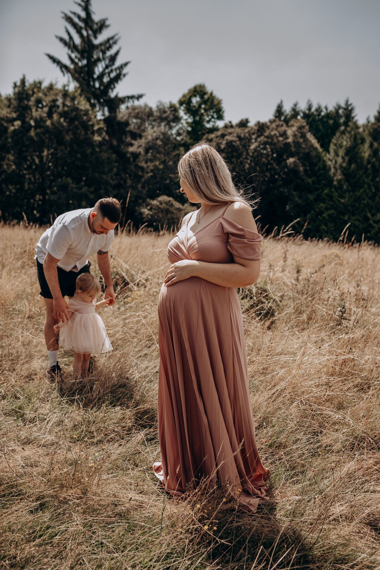 Couple poses in tall grass field during golden hour photoshoot.
