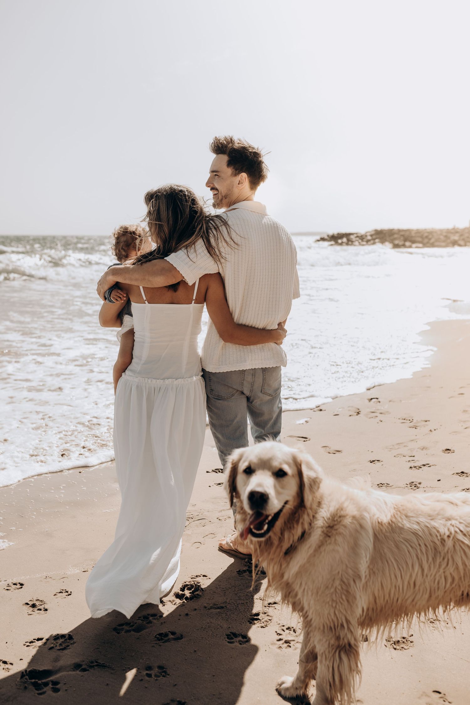 Family walking on beach with happy golden retriever dog.