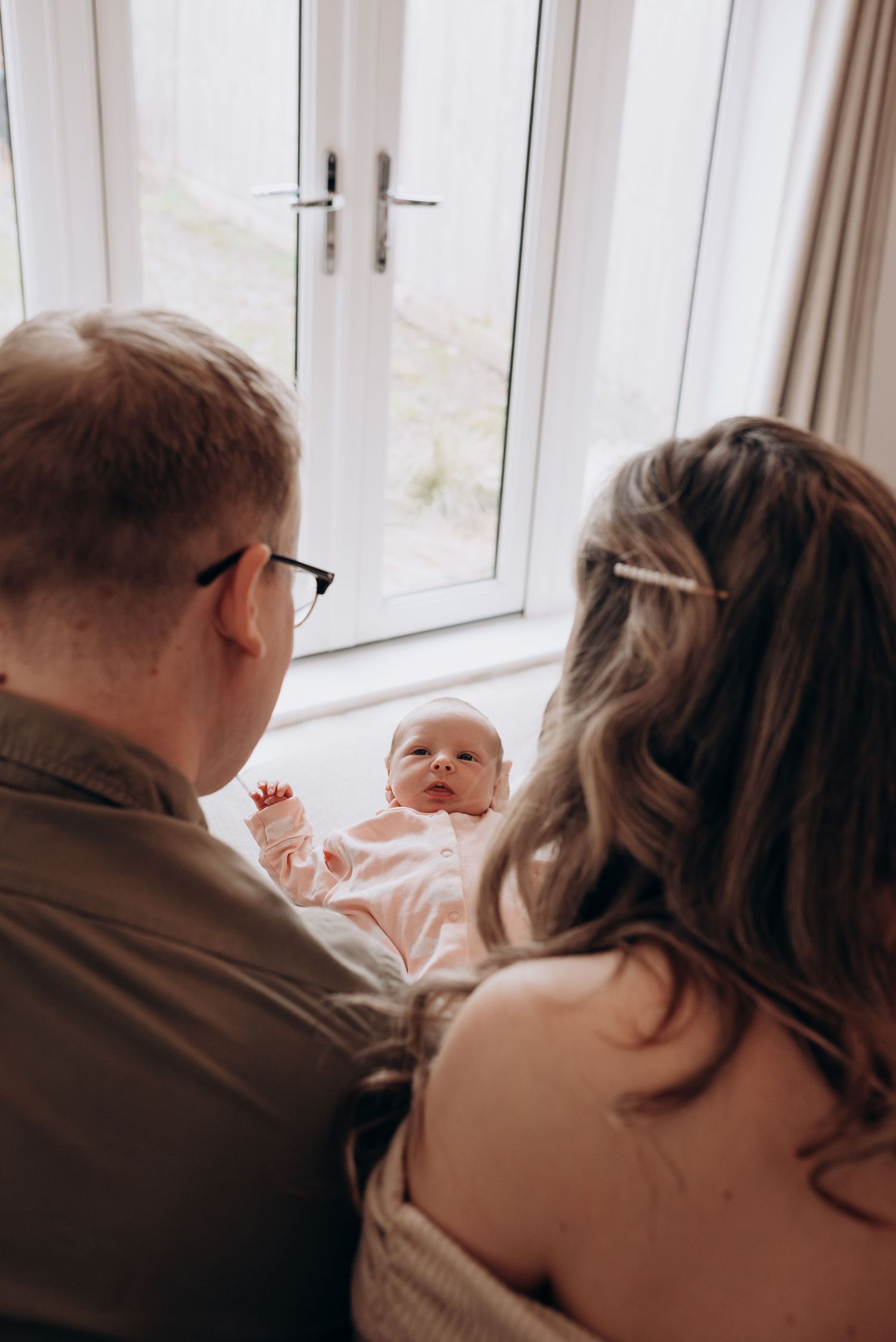 Family relaxing by bright window sharing tender moments with baby.
