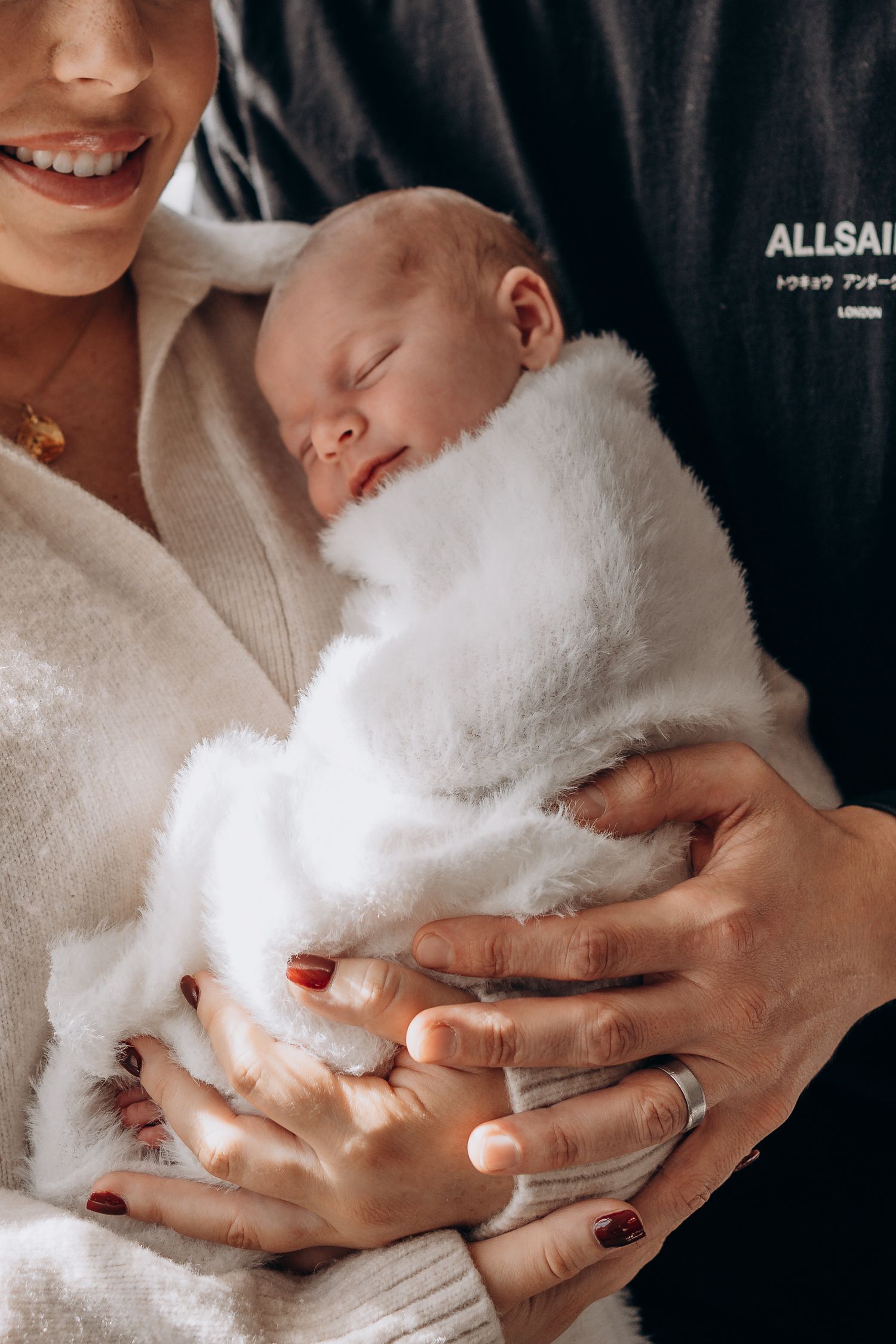 Newborn baby sleeping peacefully wrapped in white fluffy blanket, cradled in mothers arms.