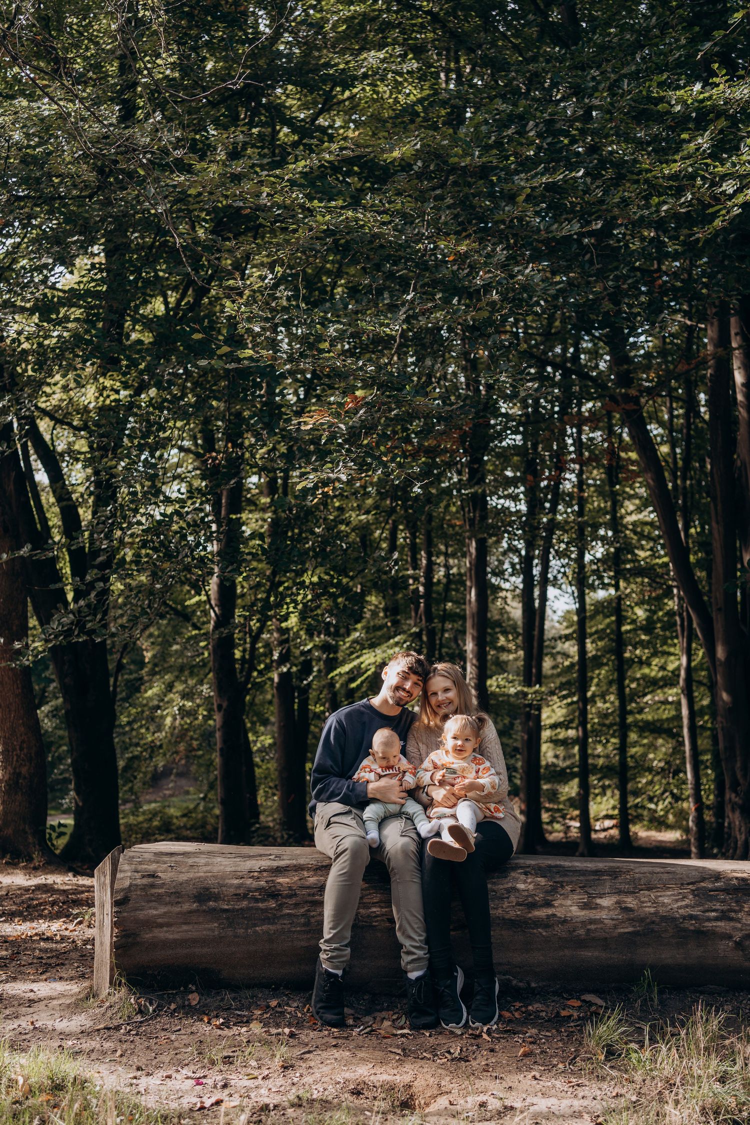 Family spending time together on fallen log in wooded area.