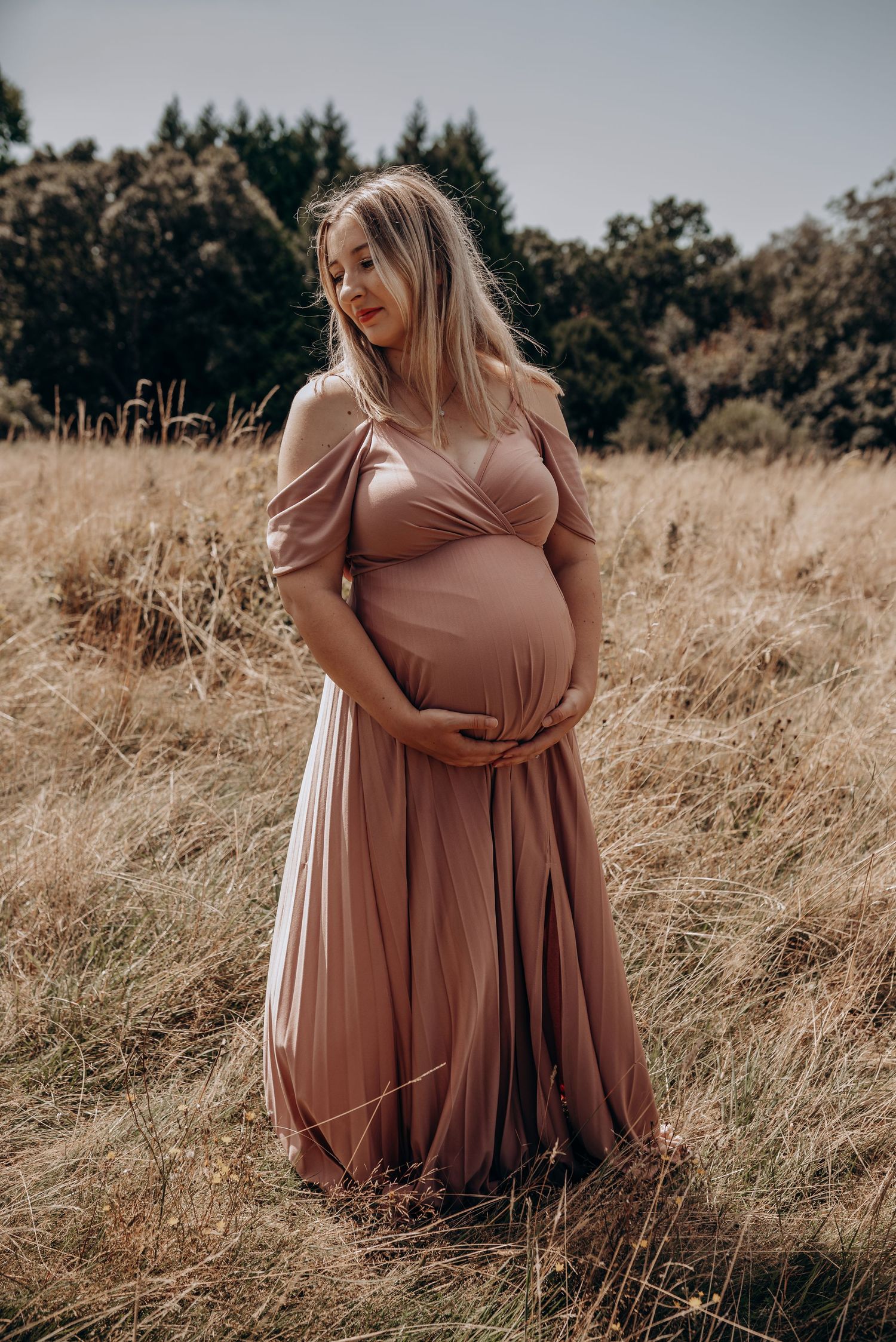 A maternity photoshoot in a golden field features a flowing dusty rose dress.