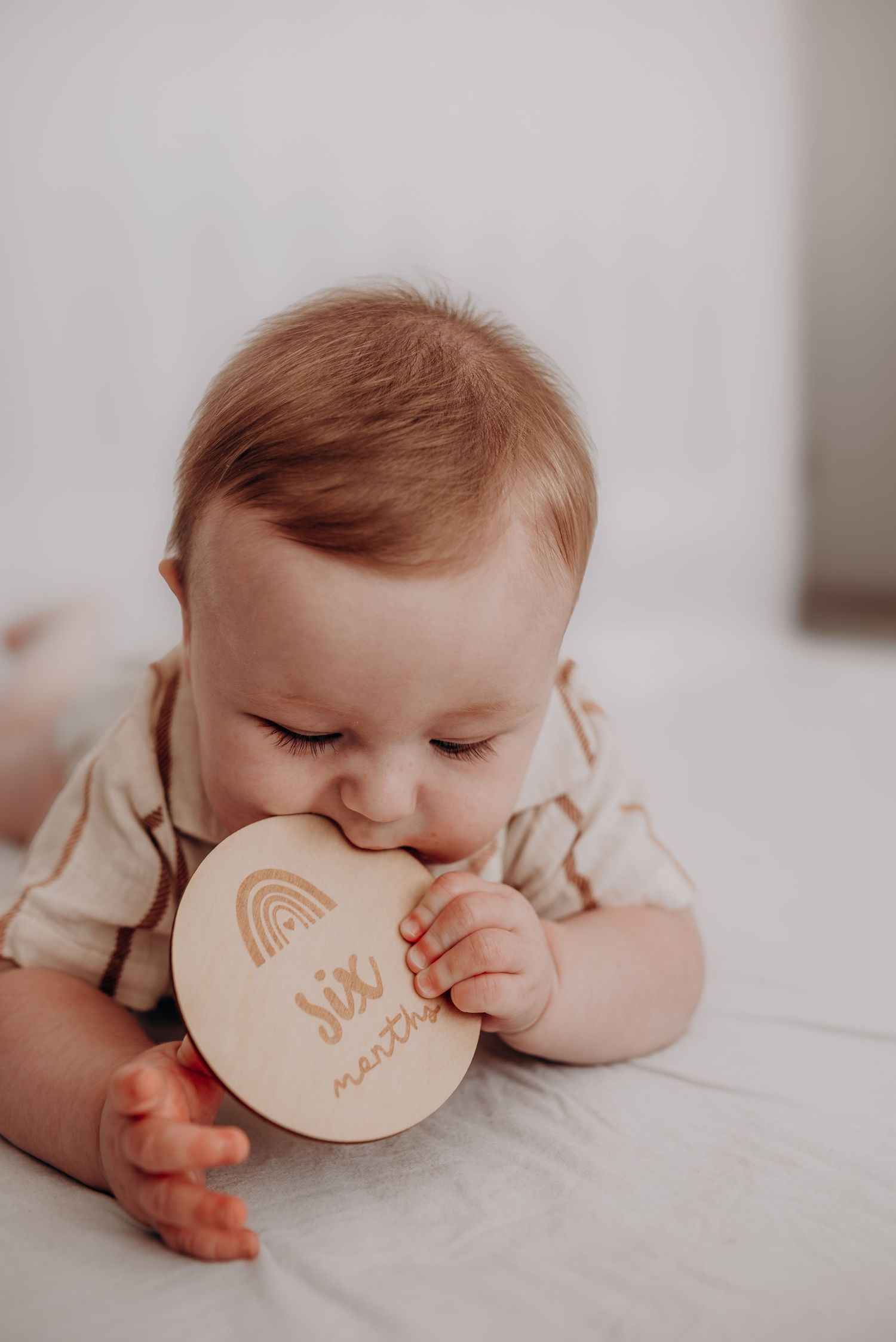 Baby lying on white surface playing with wooden rainbow teething toy.