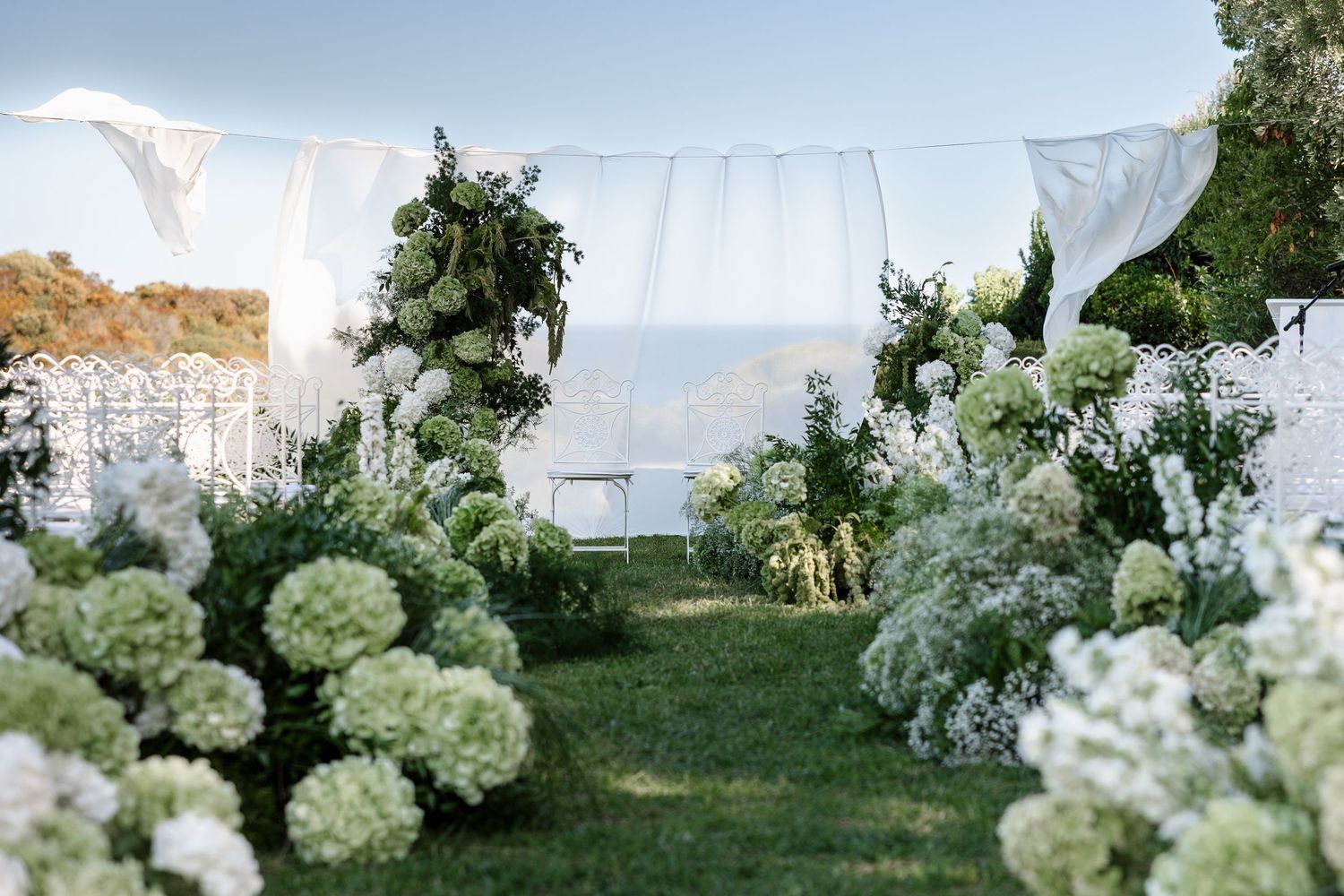 White hydrangeas and draping create an elegant outdoor wedding ceremony setting.