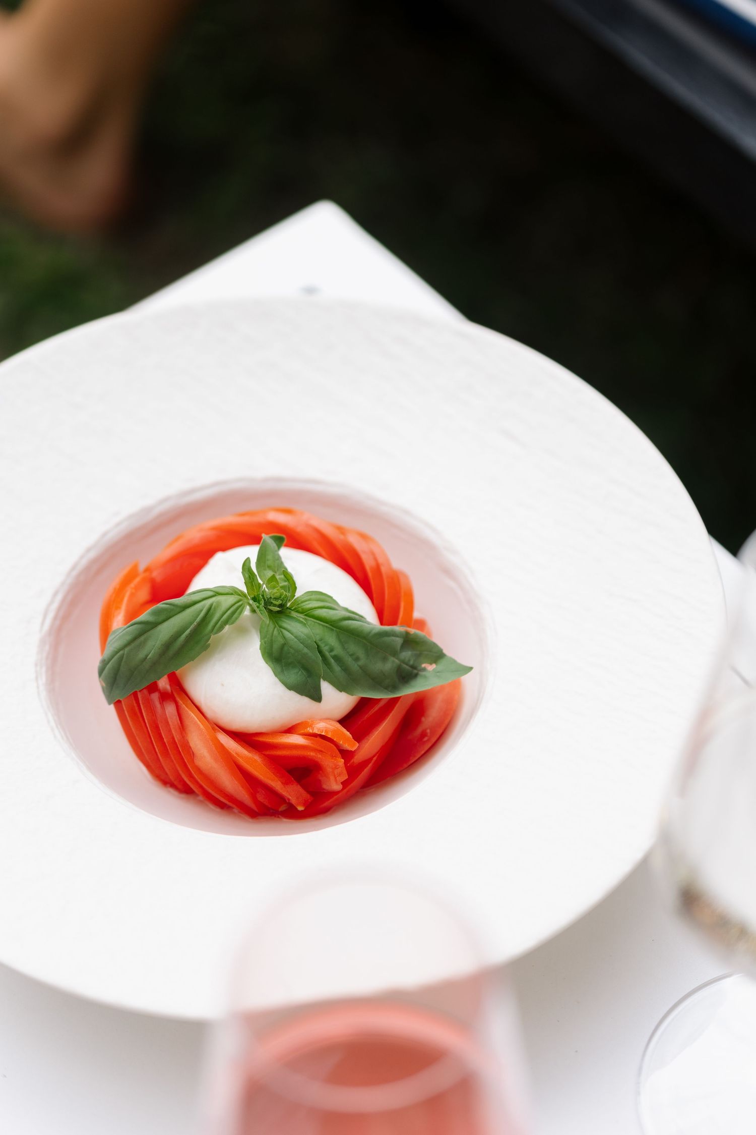Fresh caprese salad with red tomatoes and basil leaf on white plate.