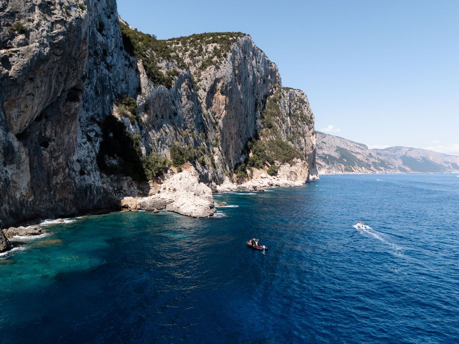 Dramatic coastal cliffs rising from turquoise Mediterranean waters on a sunny day.
