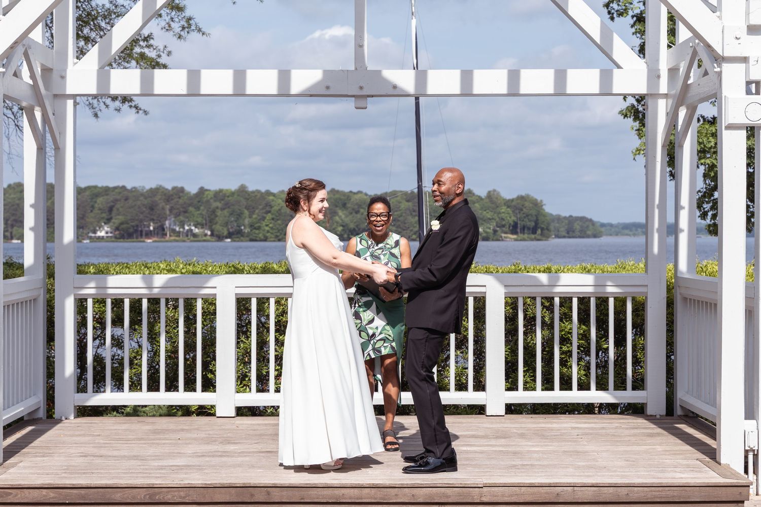 An intimate wedding ceremony takes place in a white overlooking a serene waterfront on a bright sunny day with Boathouse weddings RVA.