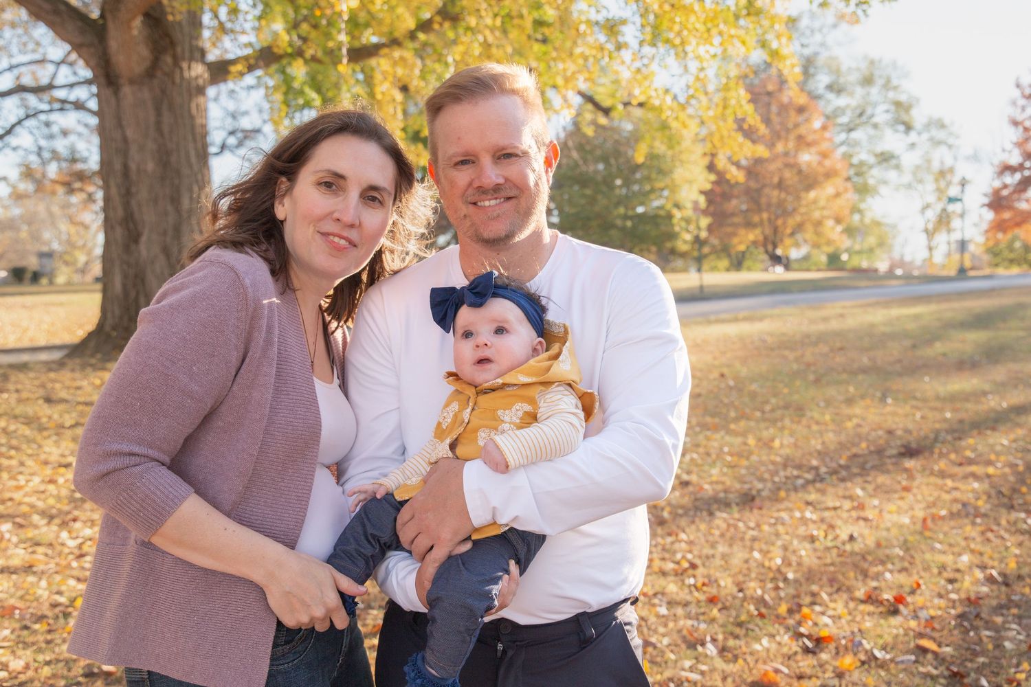 Family enjoying autumn afternoon together in park with fallen leaves and golden sunlight.