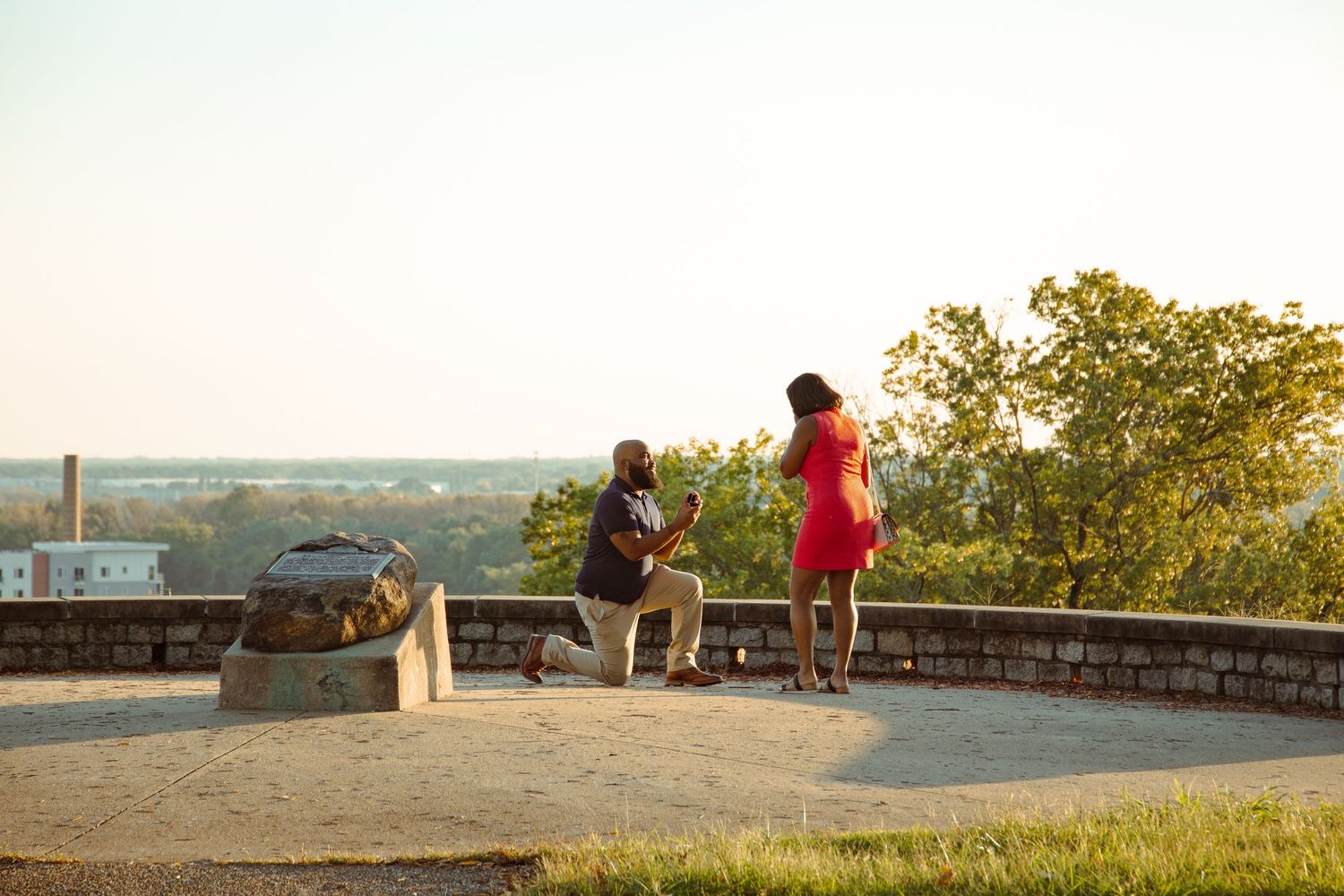 Two people stand on a hilltop scenic overlook at sunset enjoying a panoramic view of the landscape below.