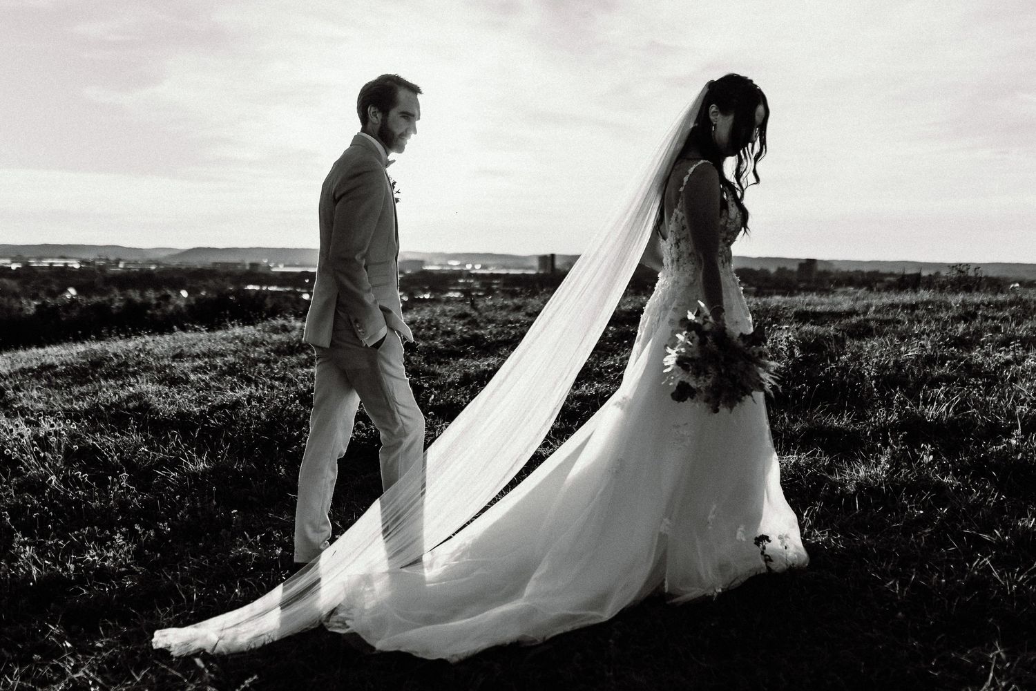 Dramatic black and white silhouette of newlyweds walking separately across a hilltop landscape.