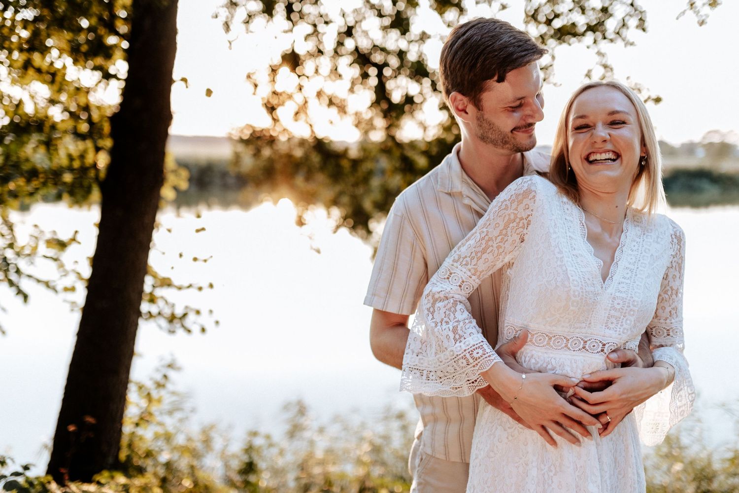A romantic sunset photoshoot by a lake with soft golden lighting filtering through trees.