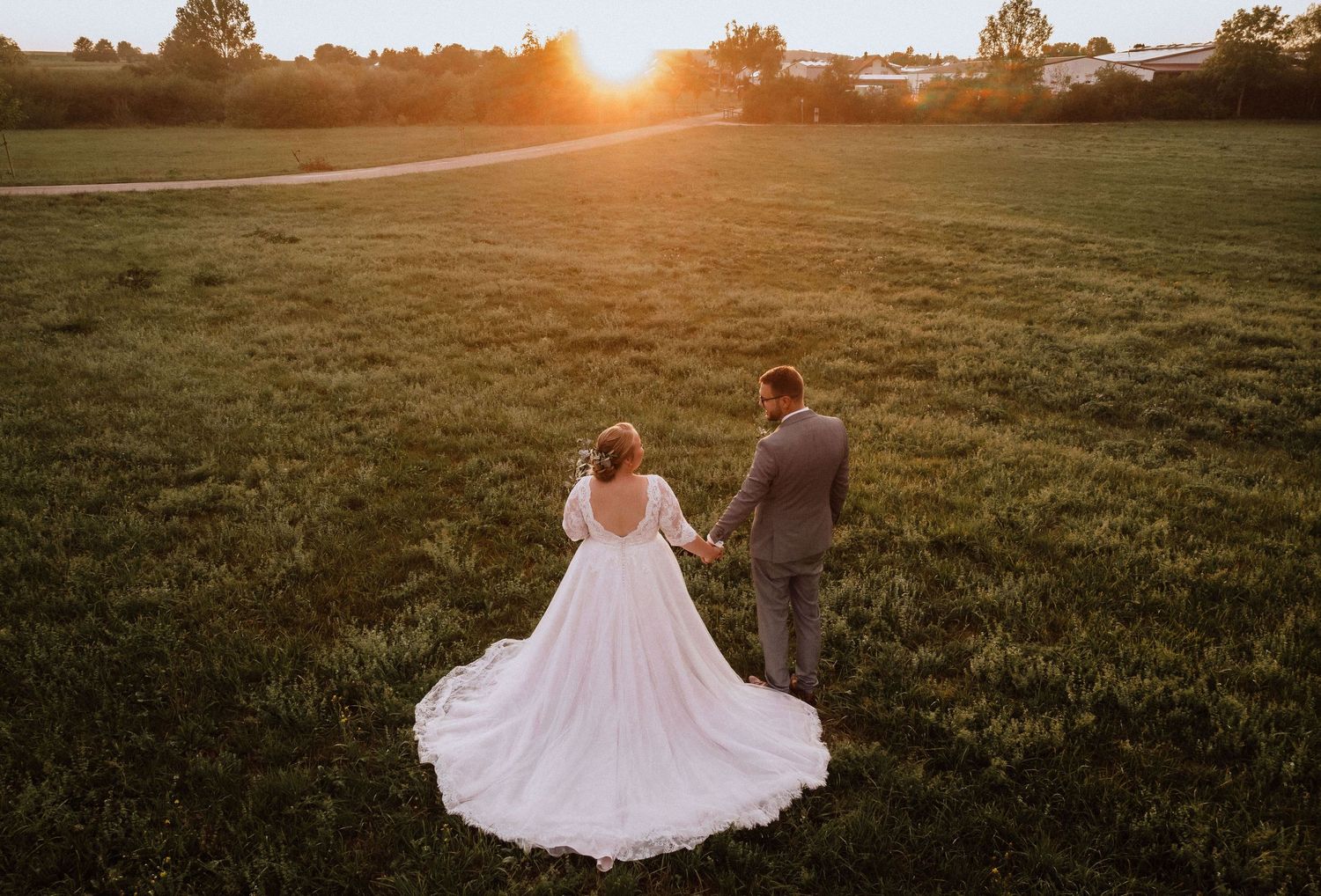 Wedding couple stands in a golden sunset field with bride's dramatic ball gown dress on display.