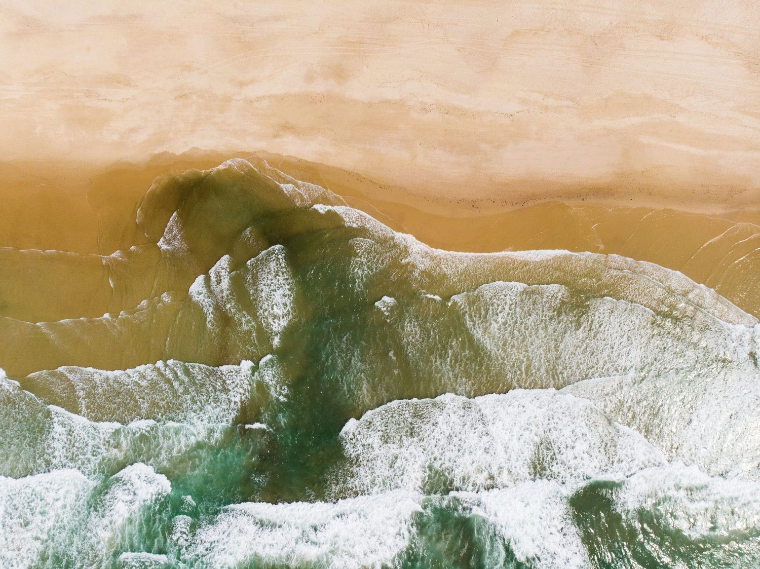 Aerial view of ocean waves creating abstract patterns in golden sunlit water.