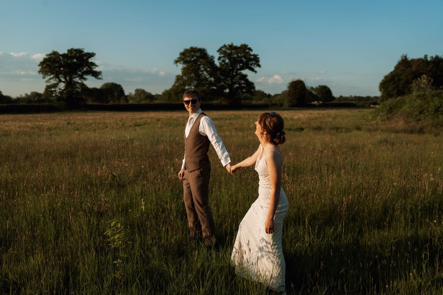 A couple walks through a golden wheat field at sunset during a romantic outdoor photoshoot.