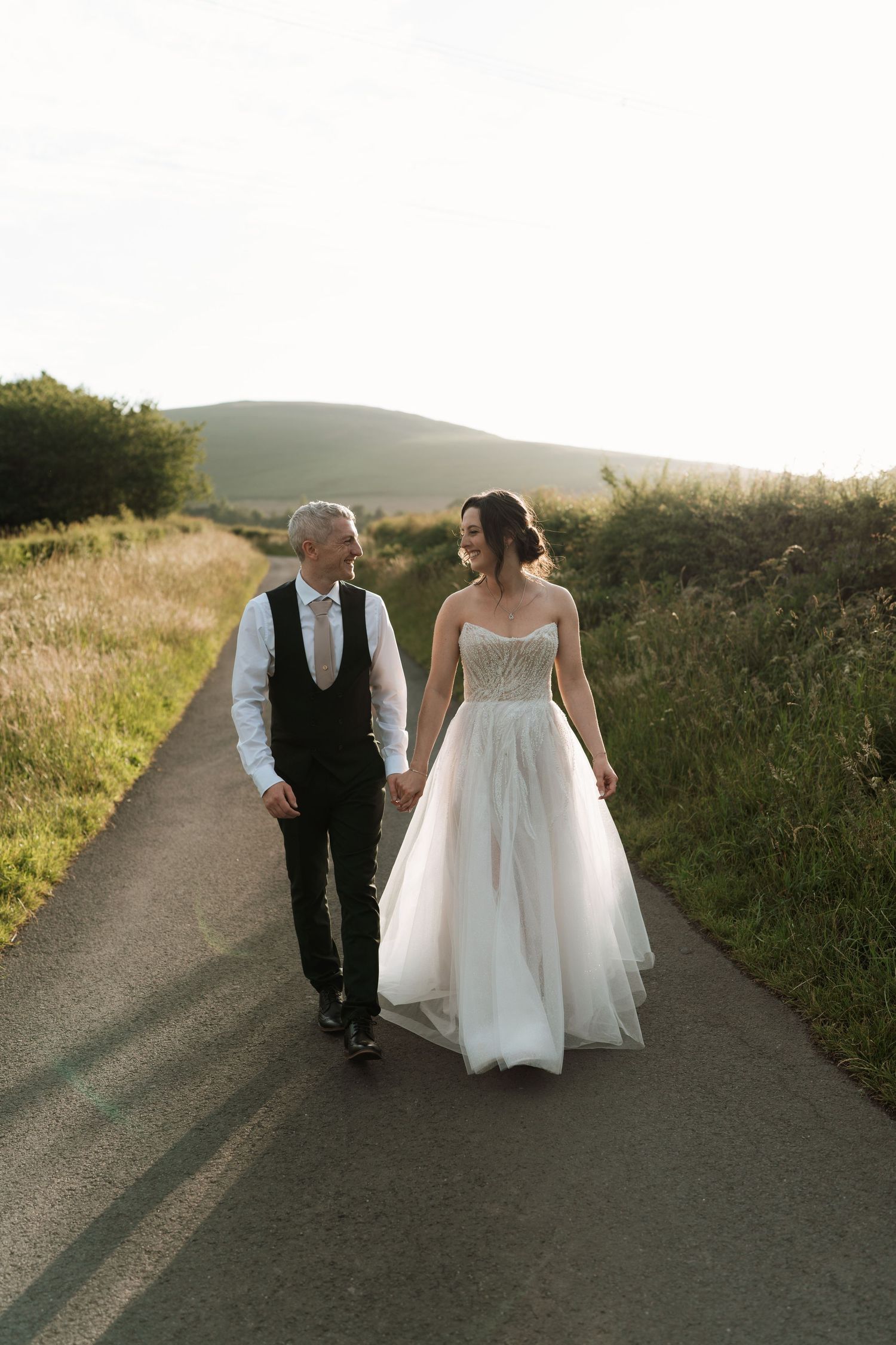 Couple in wedding attire walking together on a scenic country road at sunset, captured in multiple candid moments.