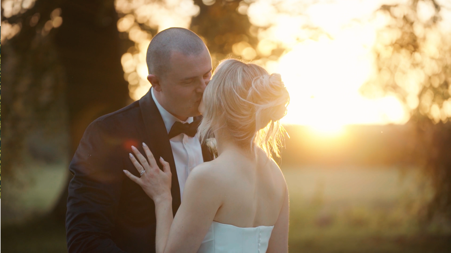 A bride and groom share an intimate moment during golden hour sunset, creating a romantic silhouette against warm light.