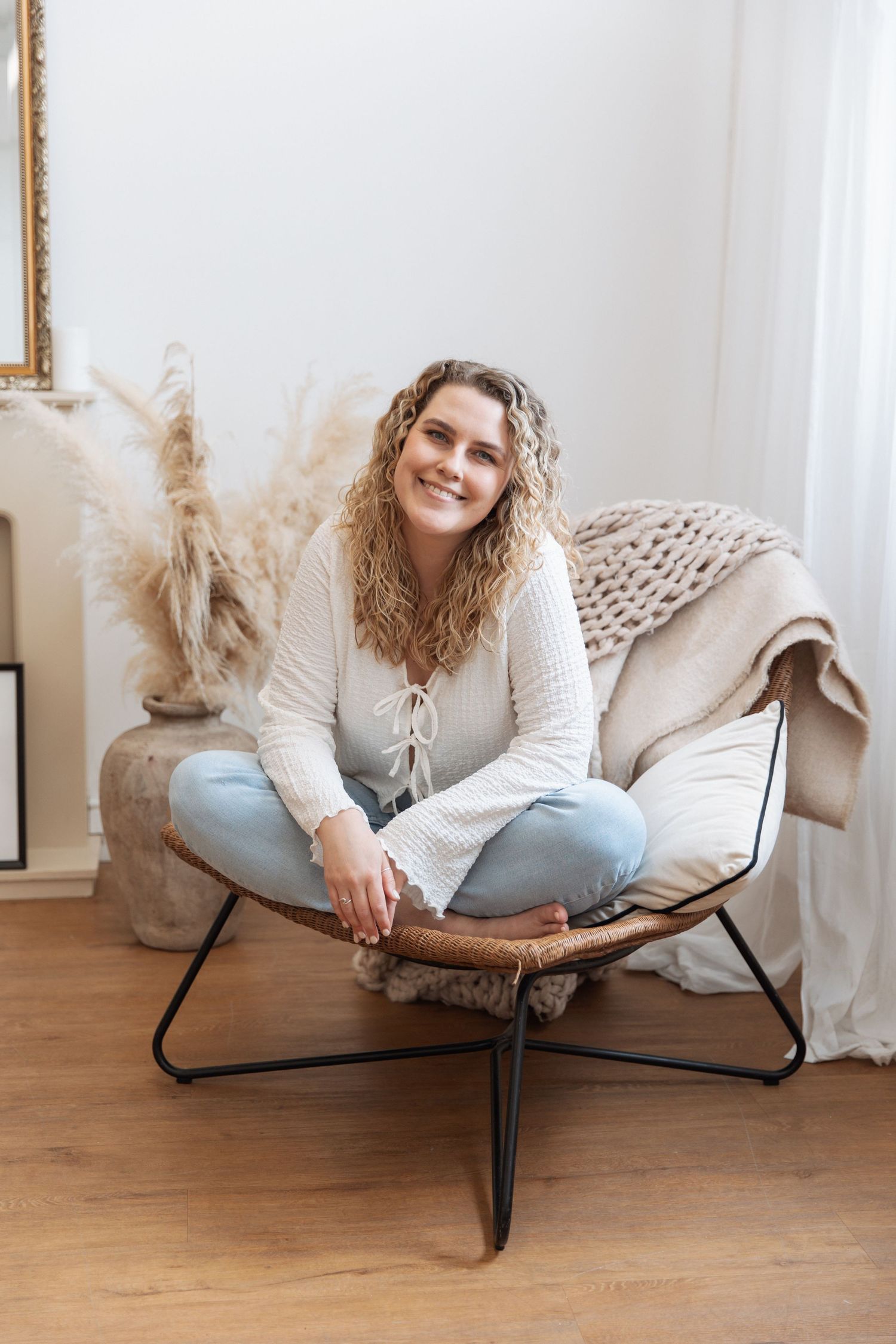 Cozy scene with someone relaxing in a modern accent chair with chunky knit throw and pampas grass decor on hardwood floor.