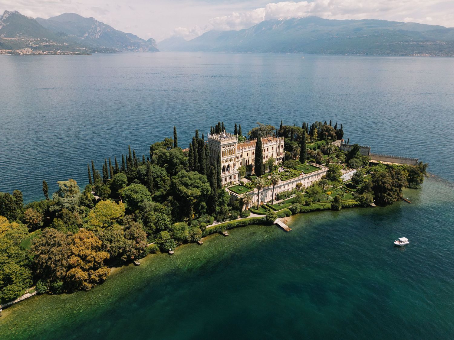 Aerial view of a scenic peninsula on Lake Garda with historic villa and lush gardens surrounded by turquoise waters.