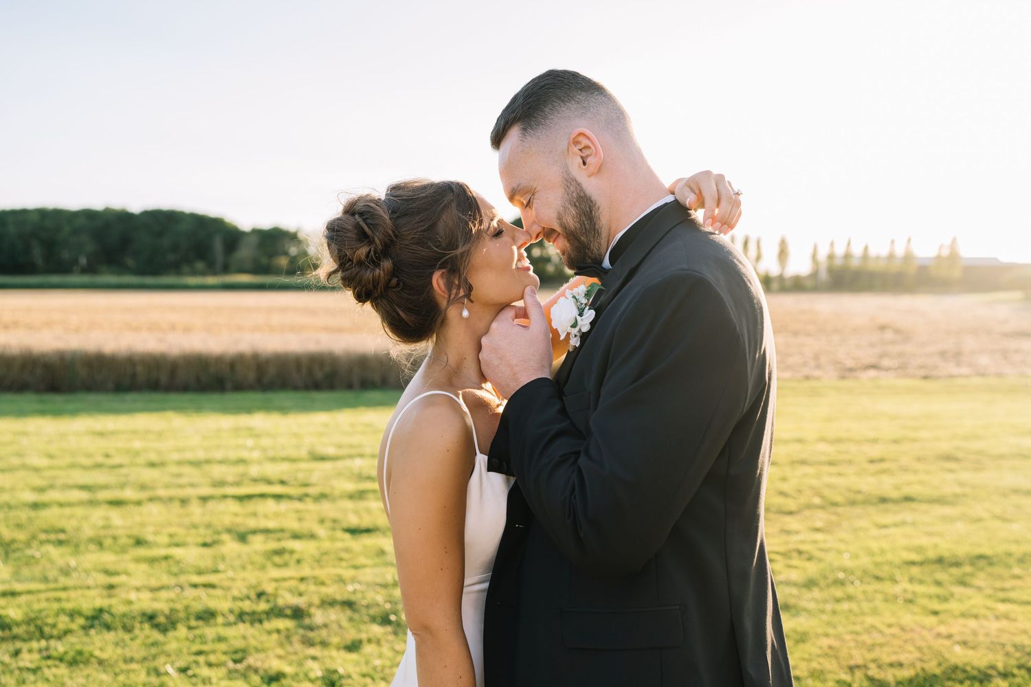 A couple shares a romantic moment in a golden sunlit field during sunset.