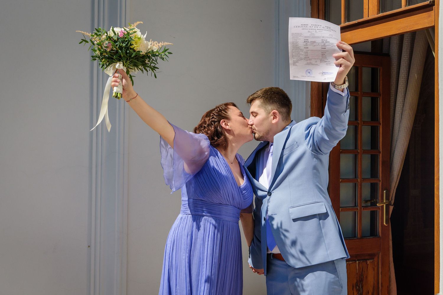 A couple in coordinating blue outfits celebrate with raised arms and joyful expressions during a special occasion.