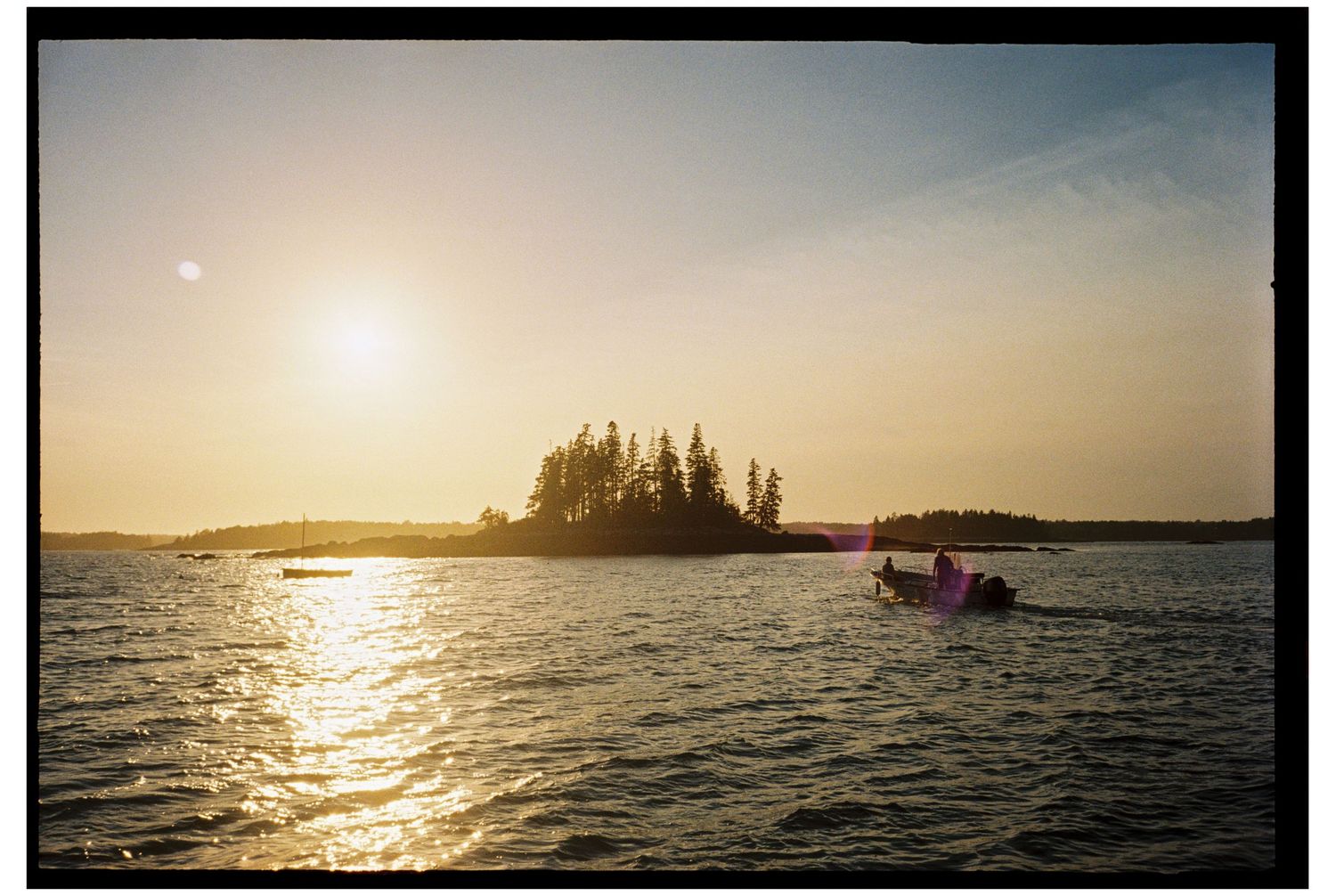 Two people on a boat during the sunset in front of a small island off the coast of midcoast Maine in the late summer on film.