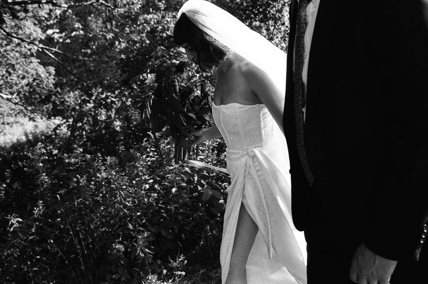 A woman walks next to her new husband through the outdoors in the late summer on a black and white film photo in Portland, Maine.
