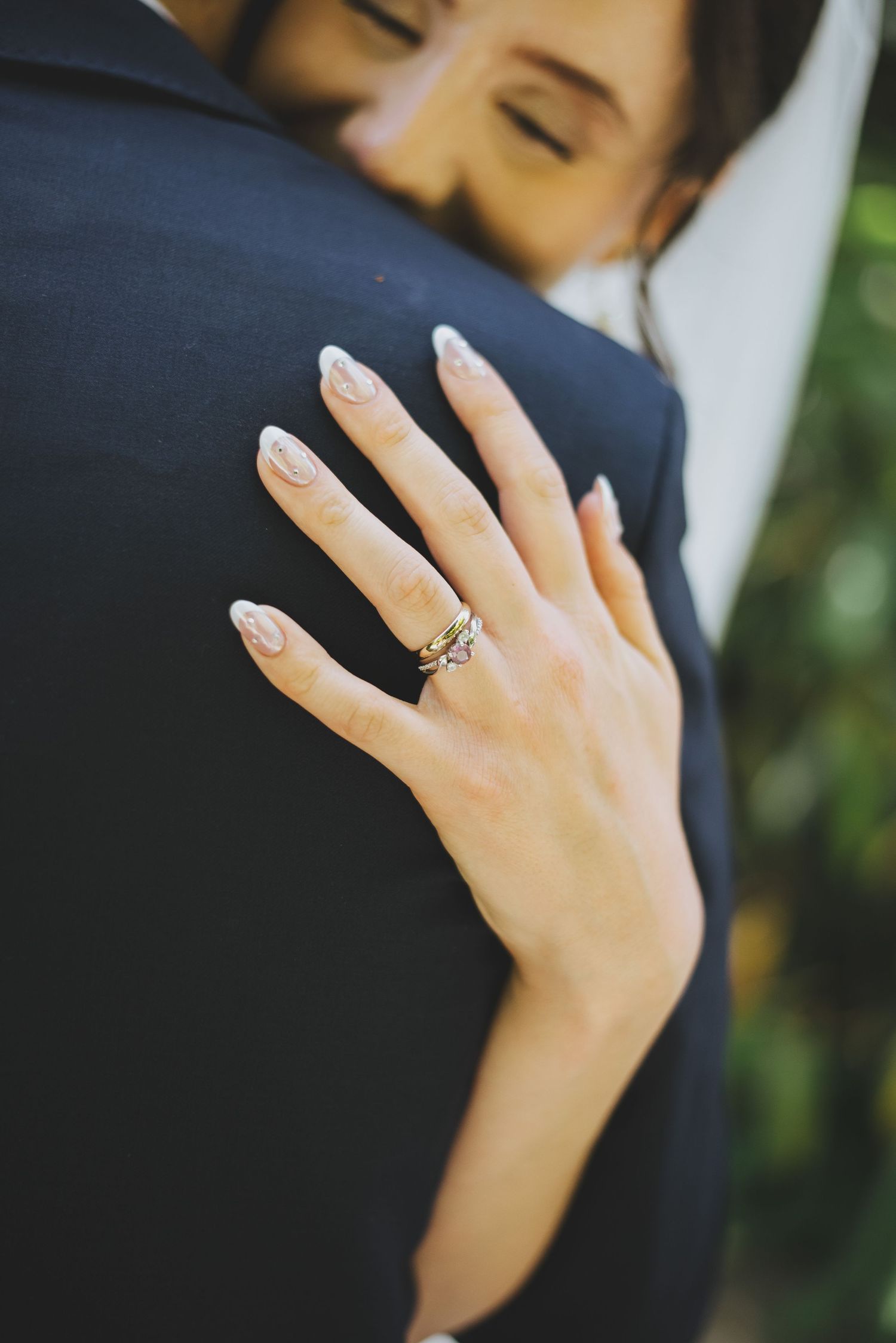 A bride's hand with a sparkling engagement ring rests on her husband's dark suit jacket.
