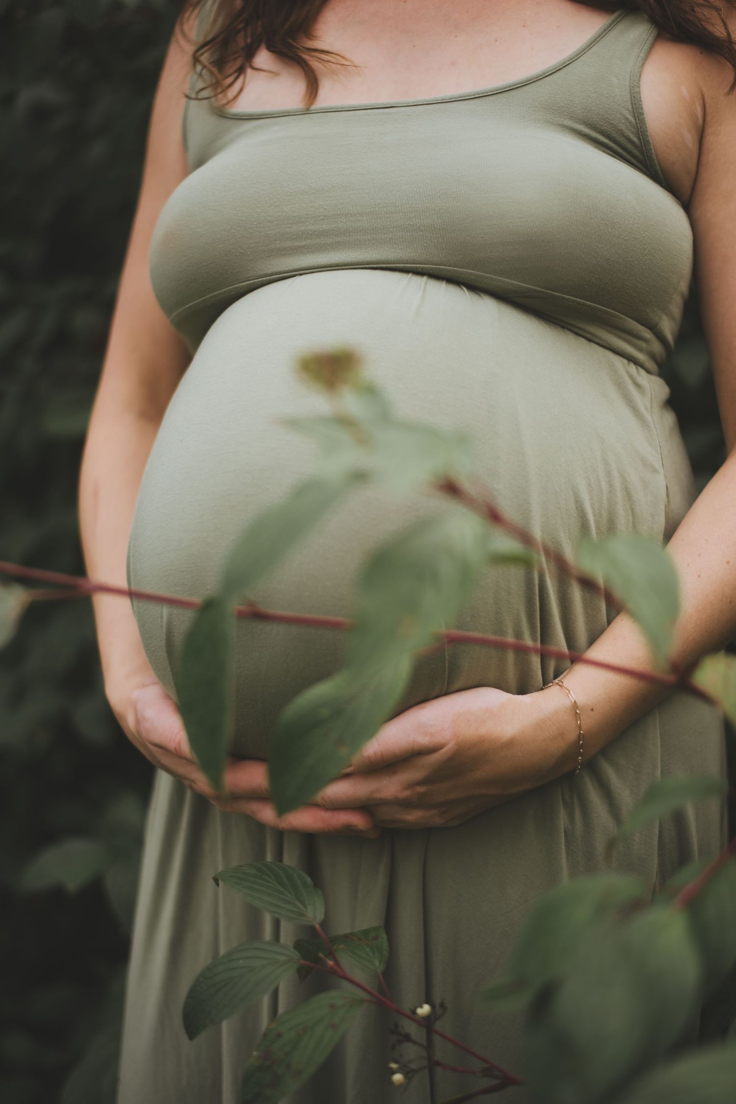 Artistic maternity photo showing pregnant belly in sage dress with foliage elements.