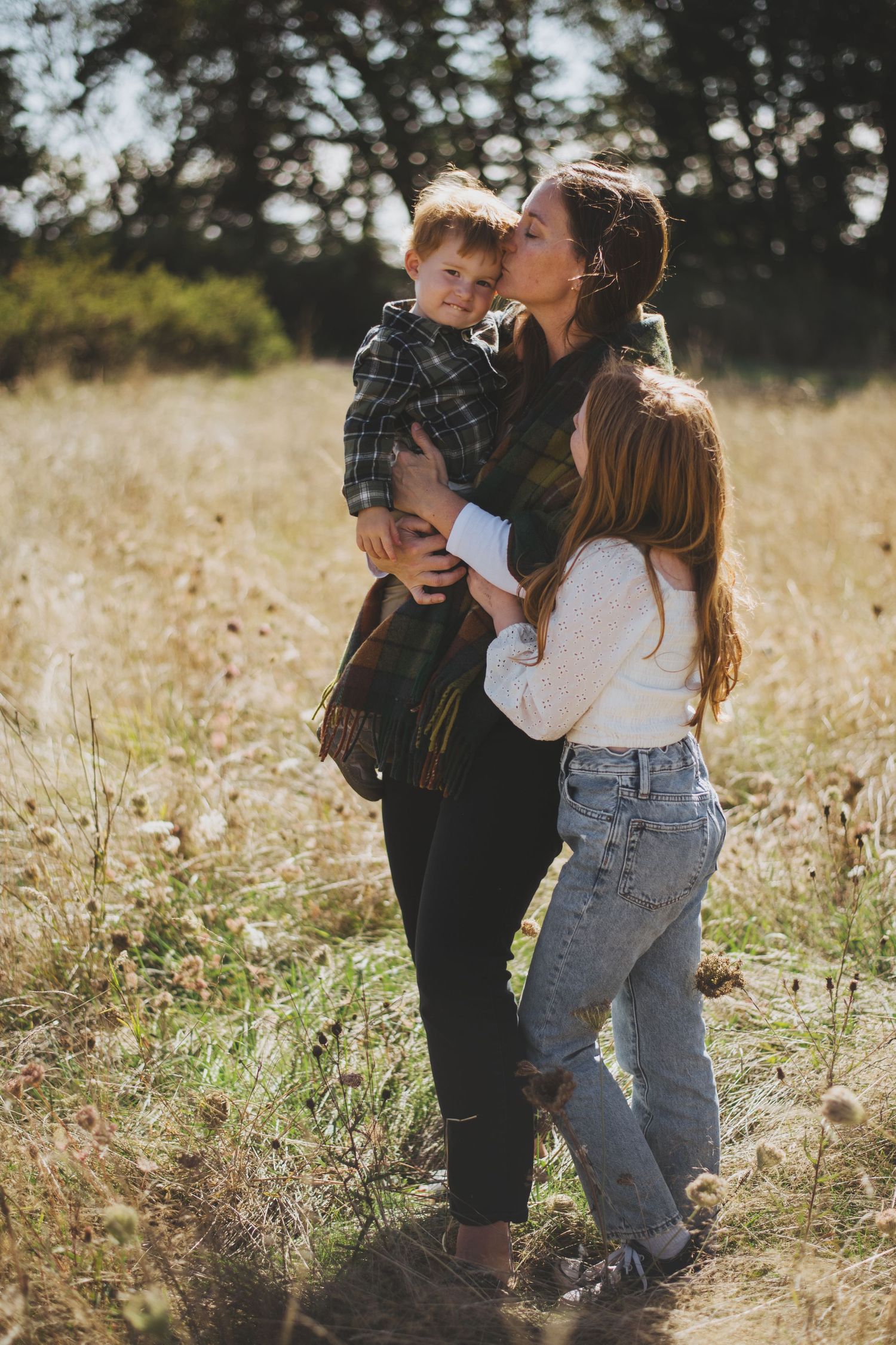 Family sharing tender moment together in sunlit golden field during outdoor photoshoot.