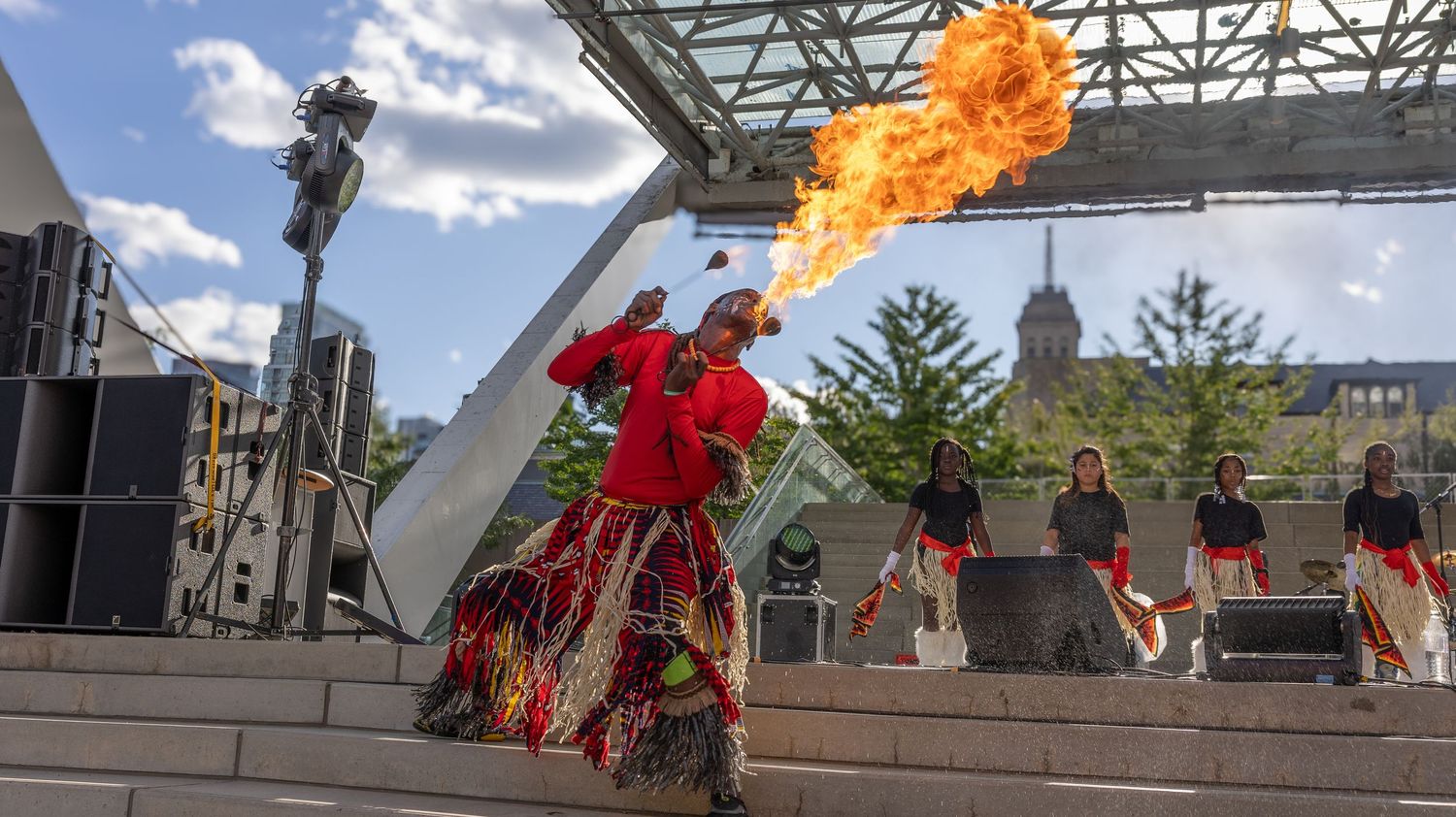 Performers in red costumes create dramatic fire effects during an outdoor theatrical performance on a stone stage.