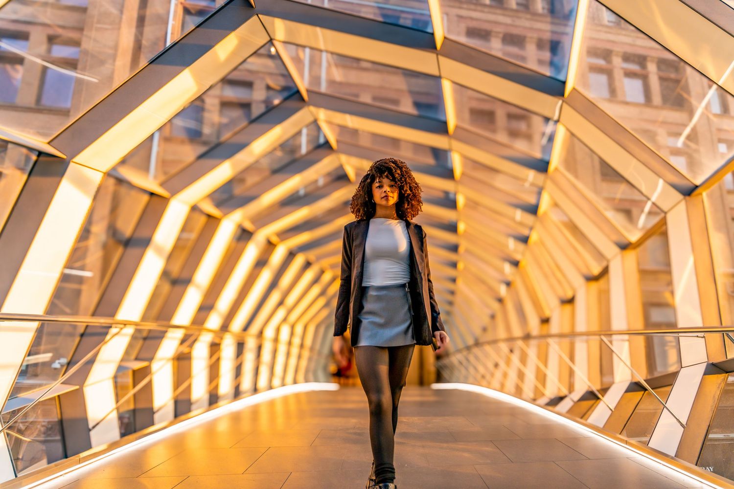 Person walking through a modern illuminated tunnel with curved wooden architecture and warm lighting creating depth.