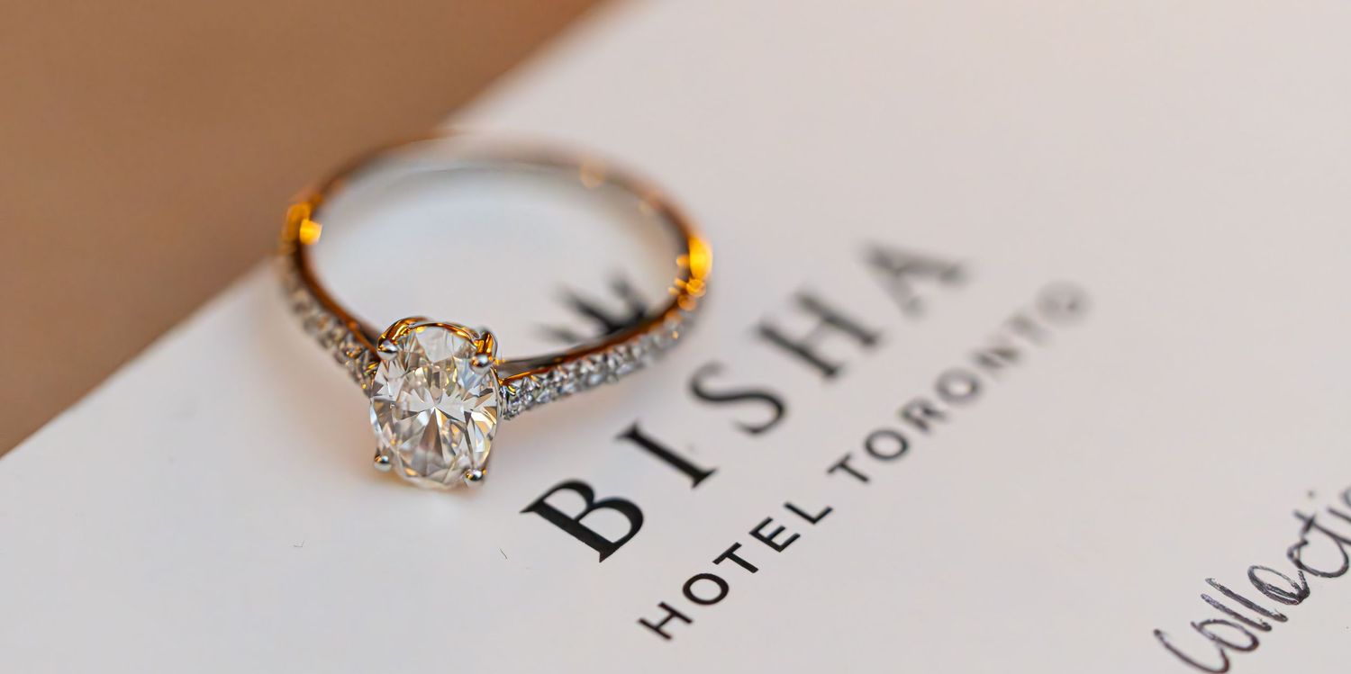 Diamond engagement ring with pavé band resting on Bisha Hotel Toronto stationery, elegant luxury jewelry close-up.