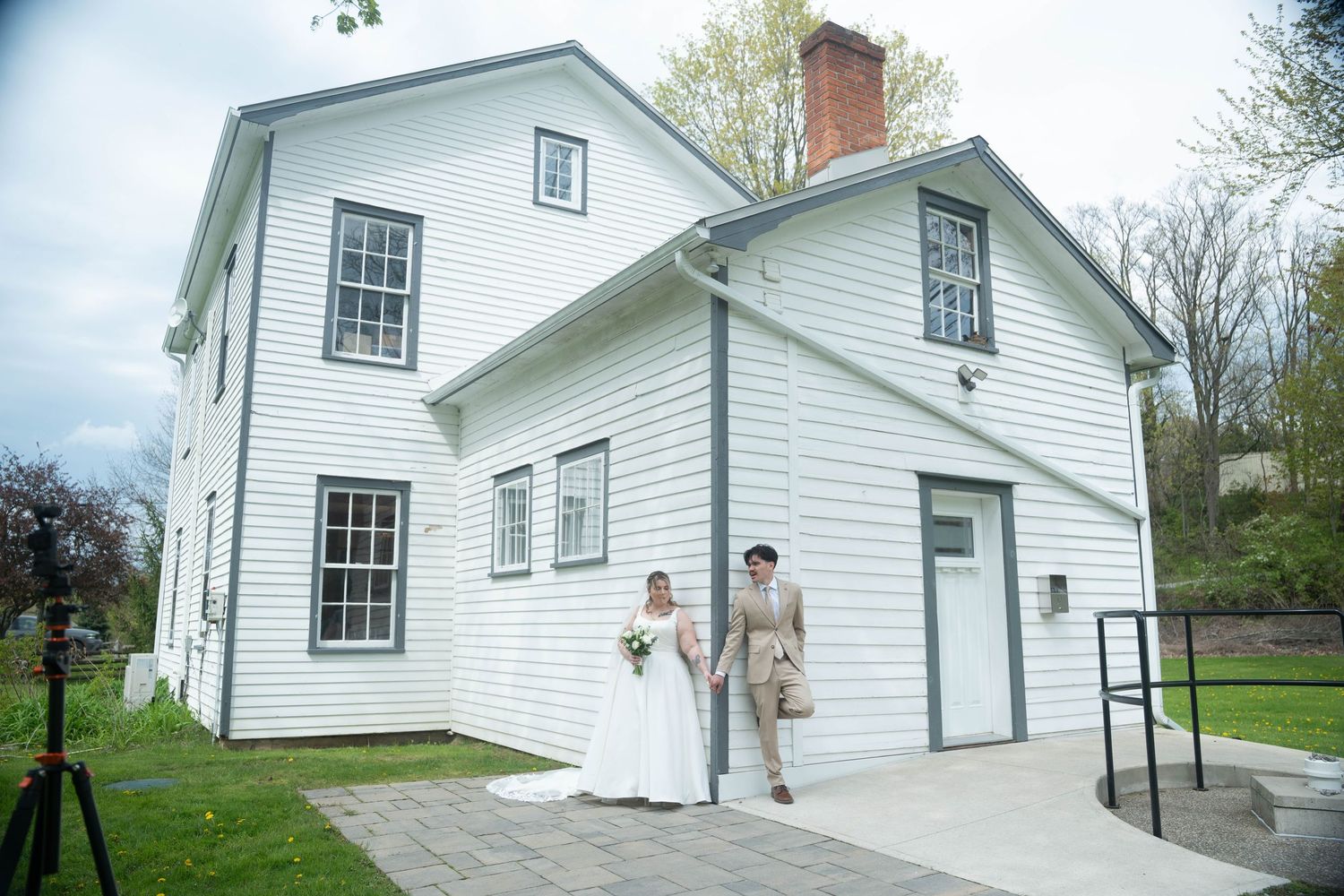 Bride and groom holding hands outside a white historic two-story building on their wedding day.