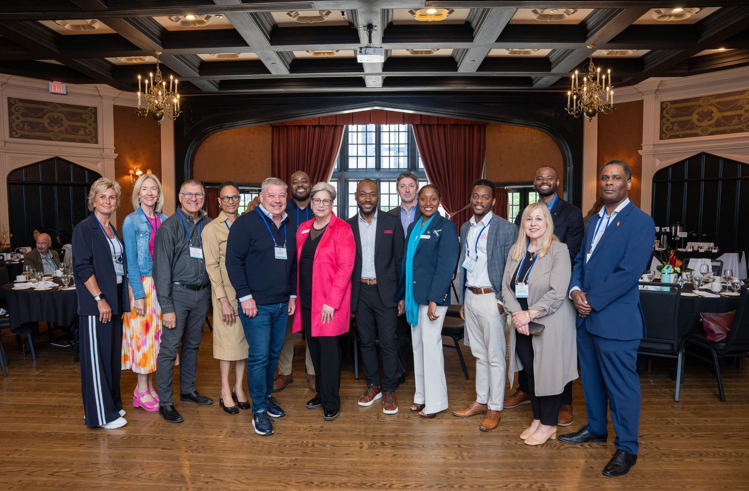 A diverse group of professionals posing together in an elegant banquet hall with coffered ceilings and chandeliers.