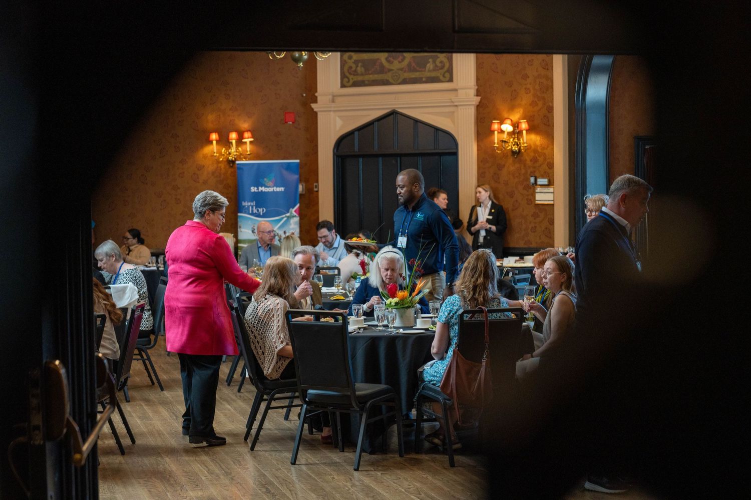 Guests mingle and dine at an elegant banquet hall event with warm lighting and floral centerpieces.