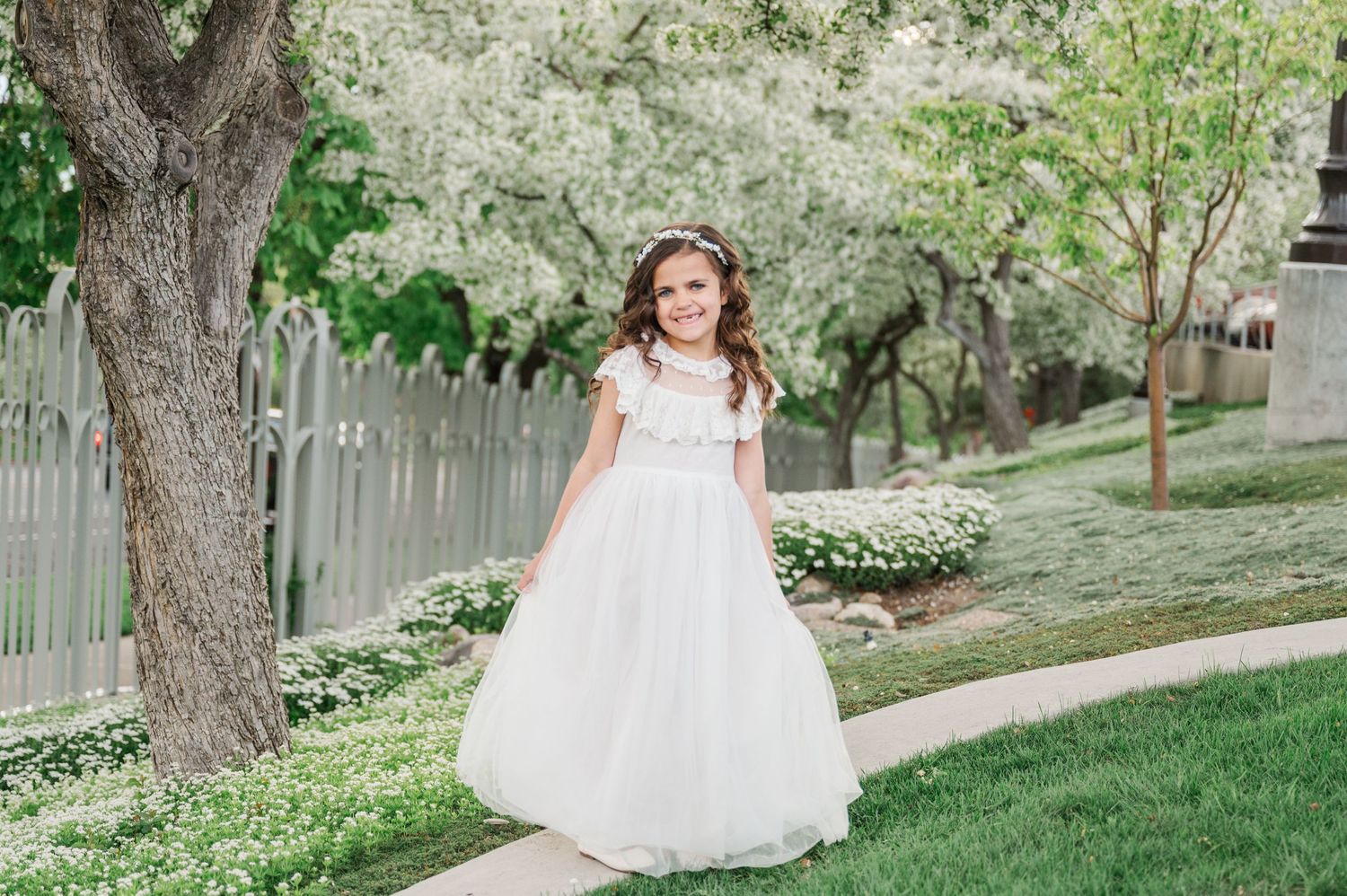 Person in white formal dress posing on garden path surrounded by spring blossoms.