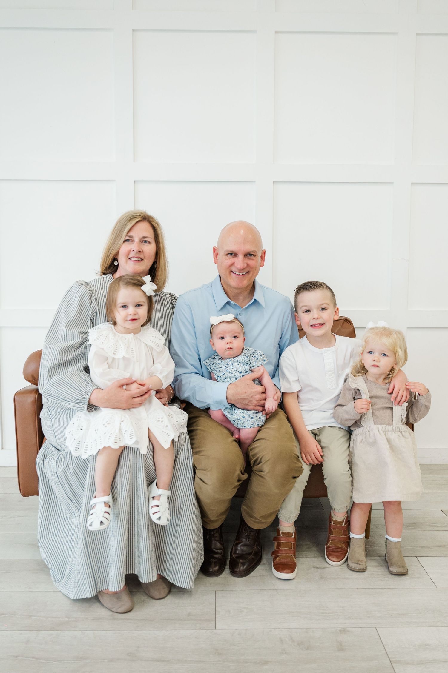 Multi-generational family portrait on bench against white paneled wall.
