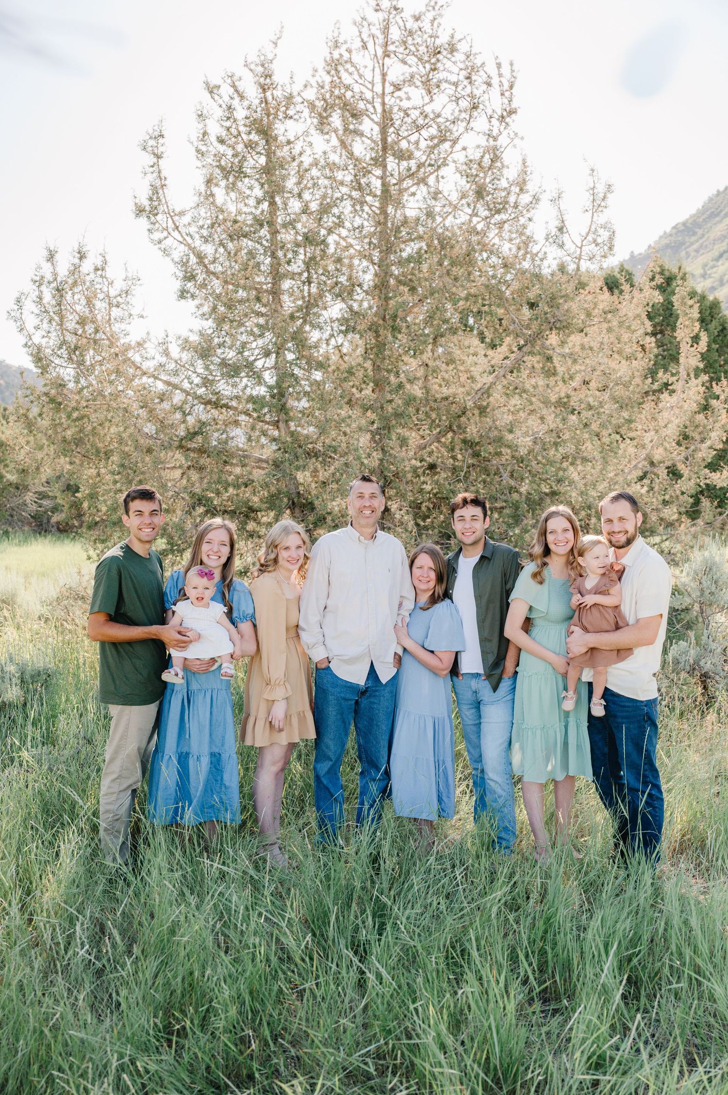 A group in coordinated blue and neutral outfits stands together in a grassy field with tall trees in the background.