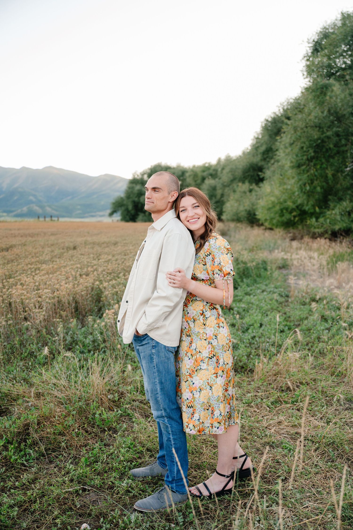 Artistically posed couple in countryside setting with mountains and fields in background.
