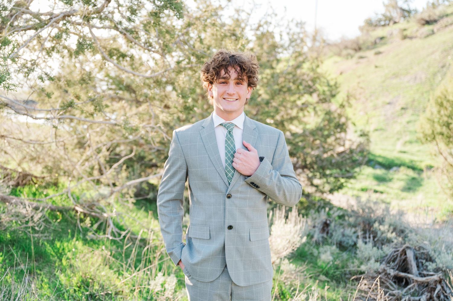 Person in grey suit standing in natural hillside setting.