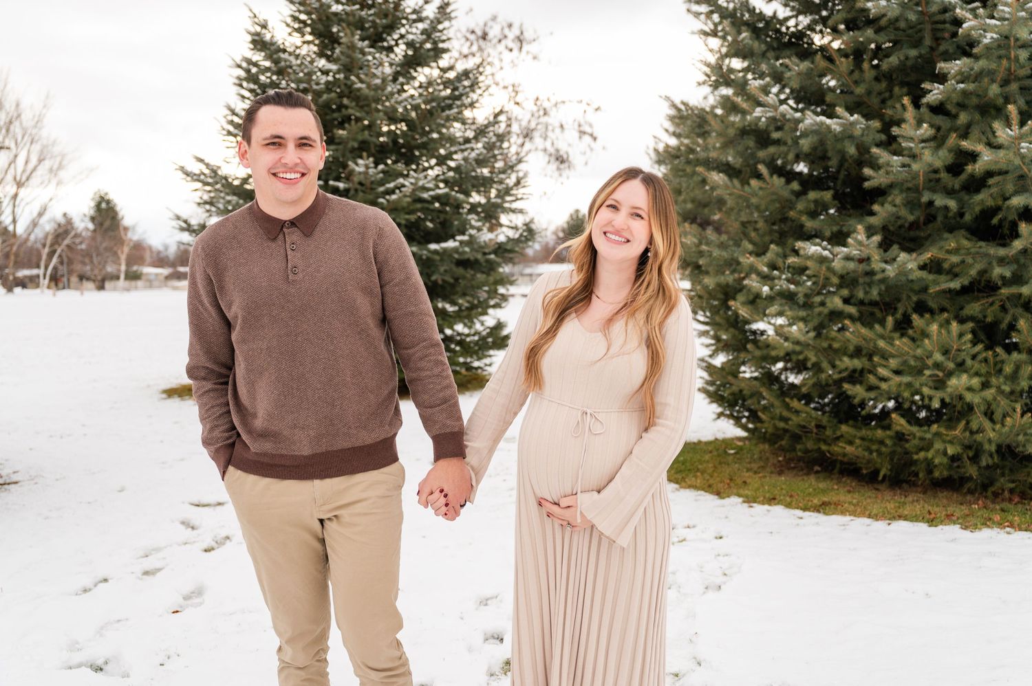 A couple holding hands while standing in a snowy landscape with evergreen trees.