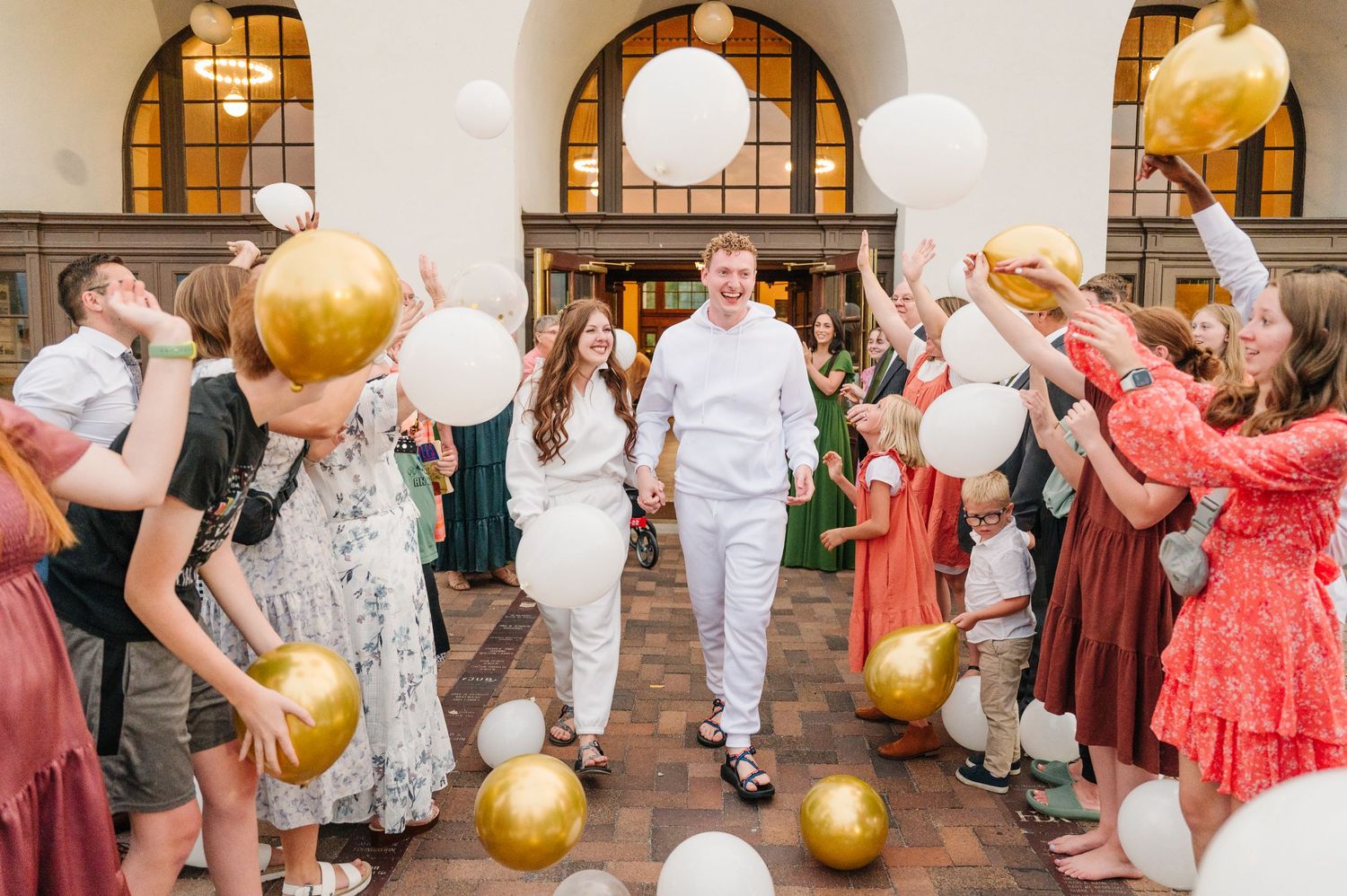 Wedding celebration with guests holding gold balloons in an arched hallway.